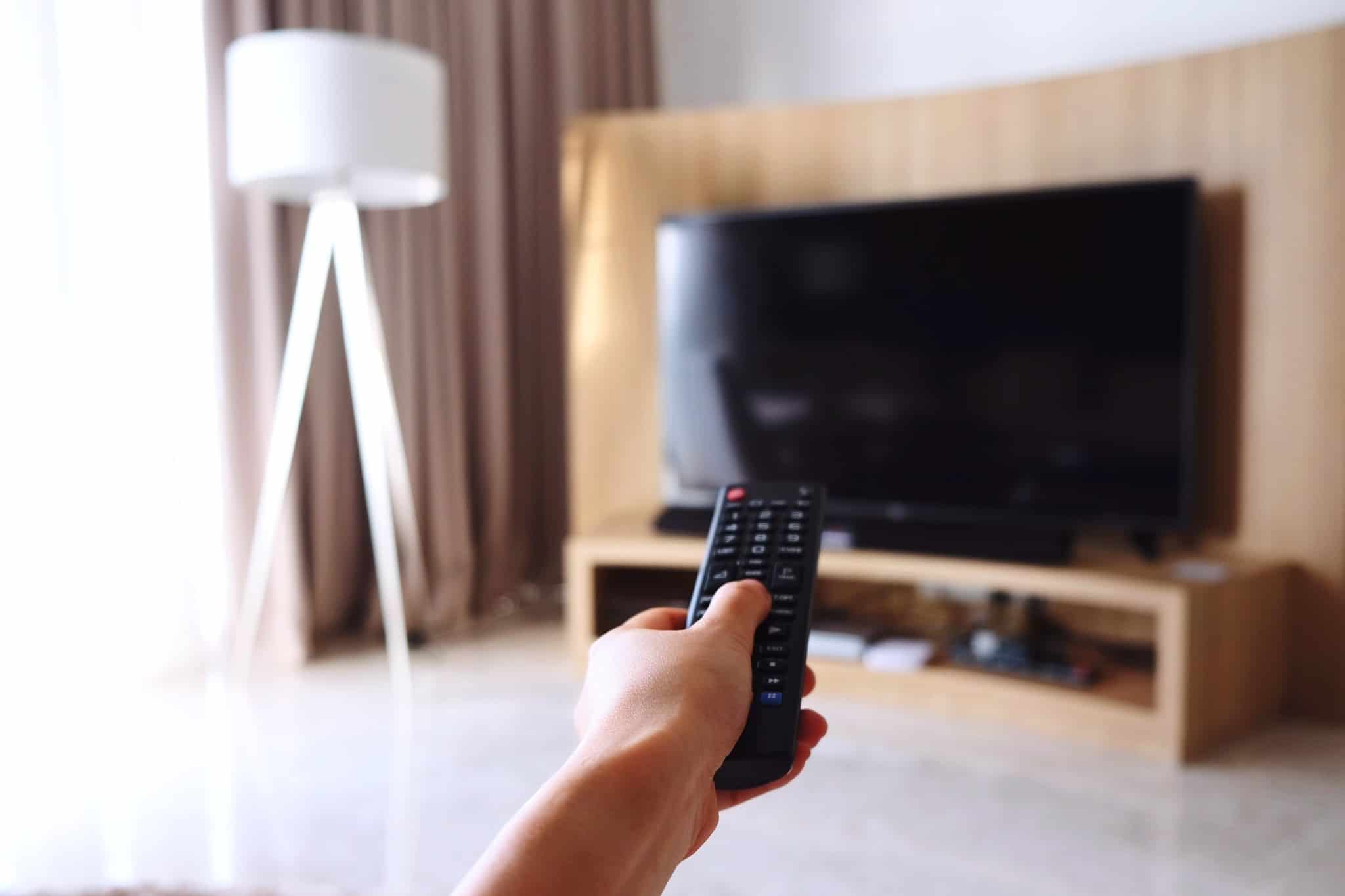 pessoa a pegar no comando e a apontar para a televisão