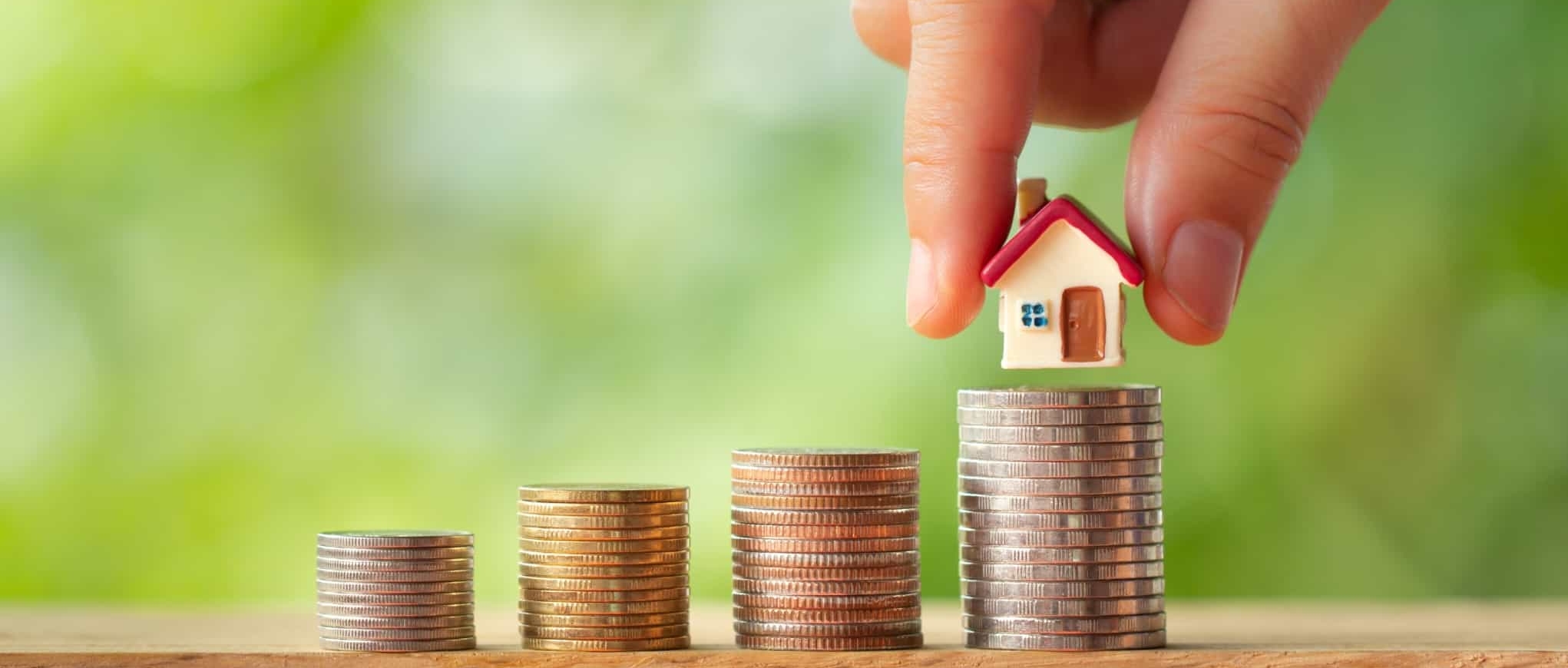 mão a colocar uma casa miniatura numa pilha de moedas