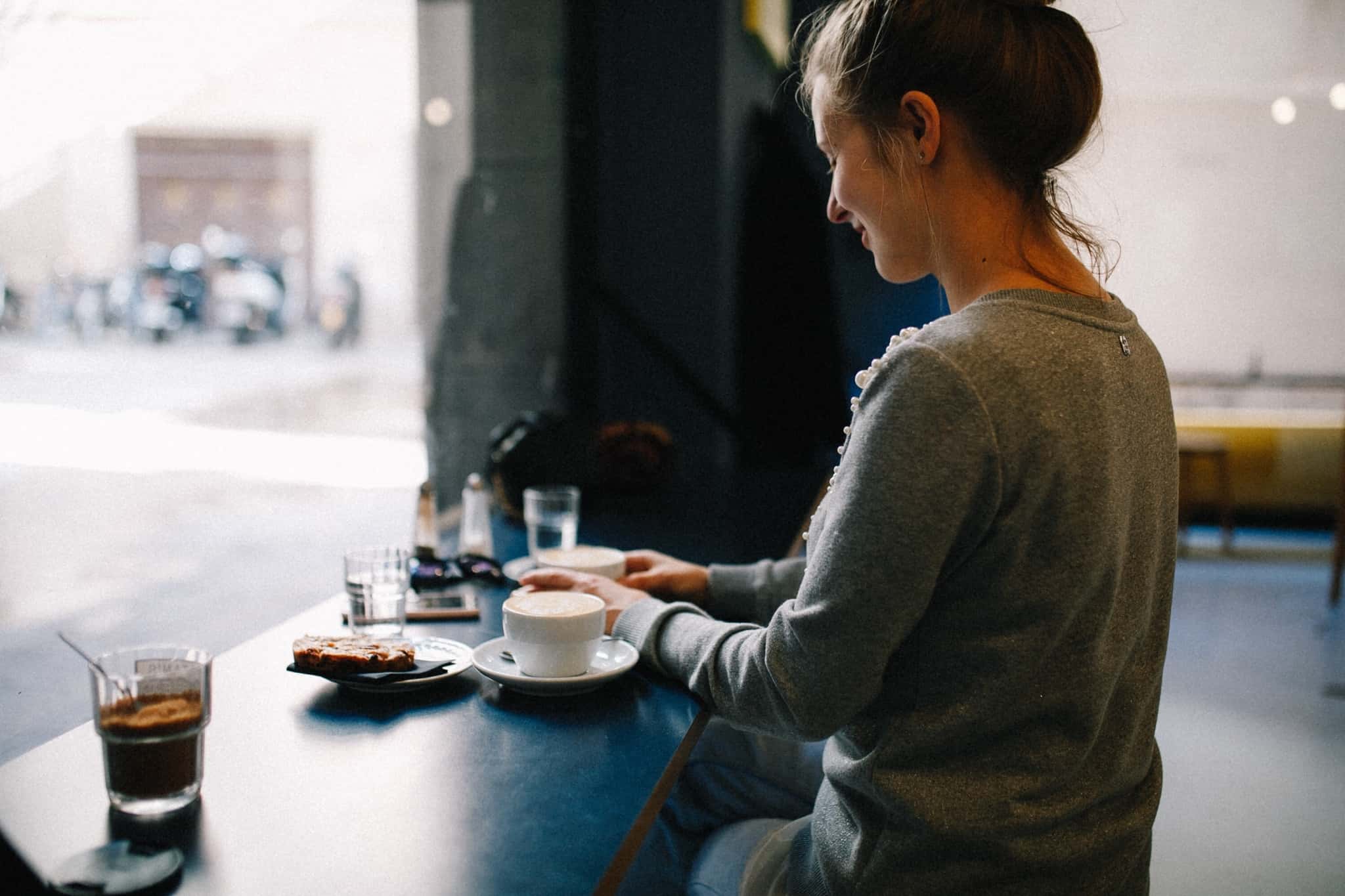 Rapariga num café a comer e a beber enquanto mexe no telemóvel