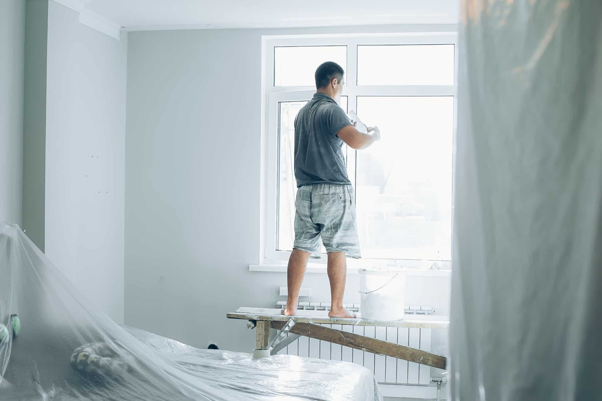 Homem está a pintar o interior de uma casa, junto a uma janela