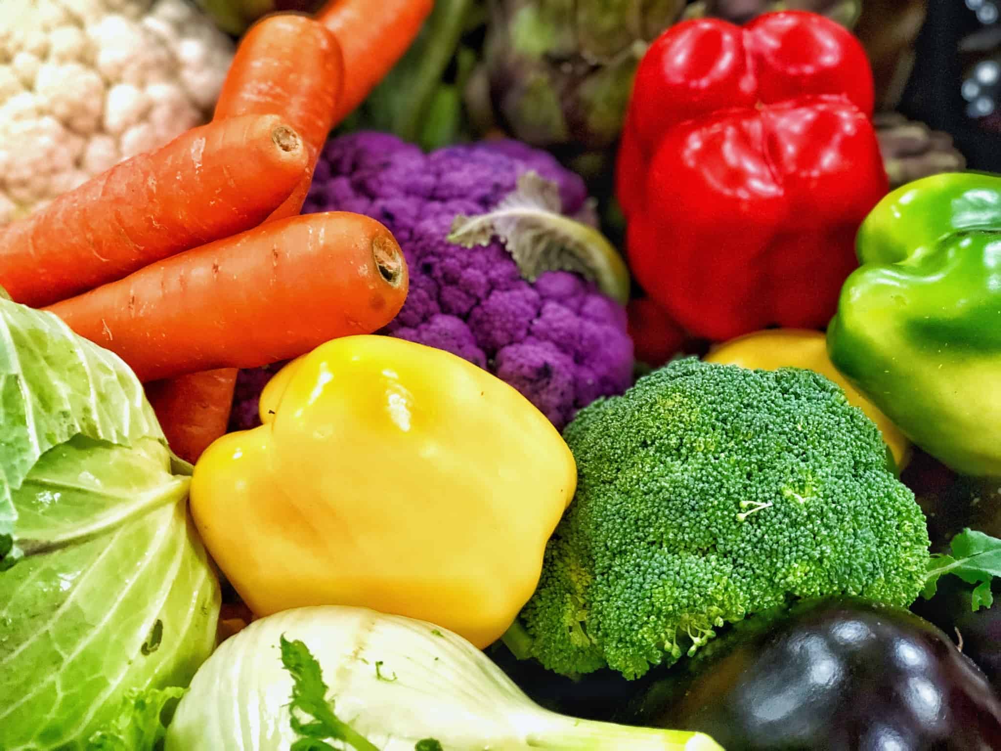 Vários legumes dispostos, como cenoura, pimentos, bróculos, couve