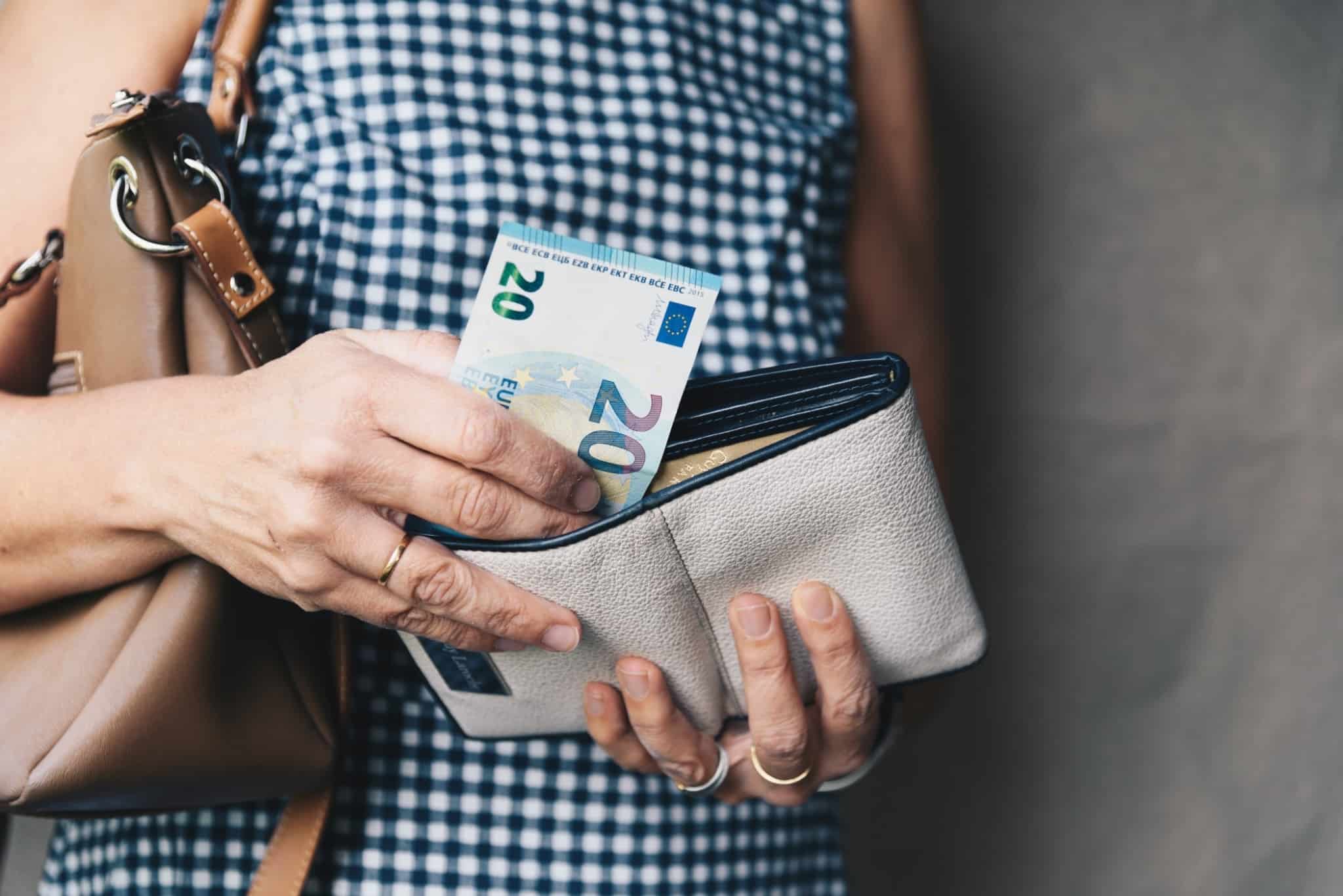 mulher a abrir a carteira e a retirar notas de vinte euros