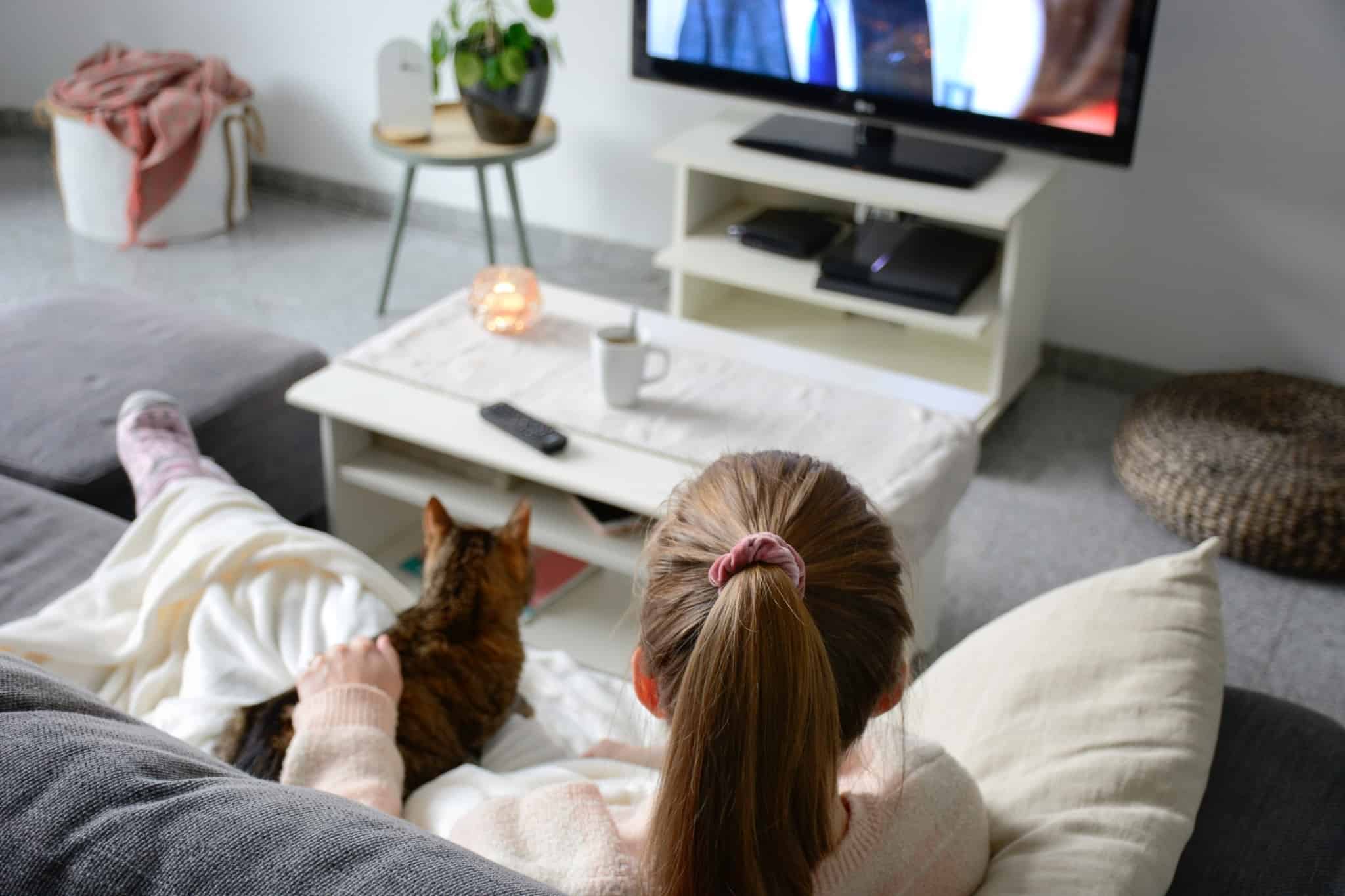 rapariga com um gato ao lado a ver televisão