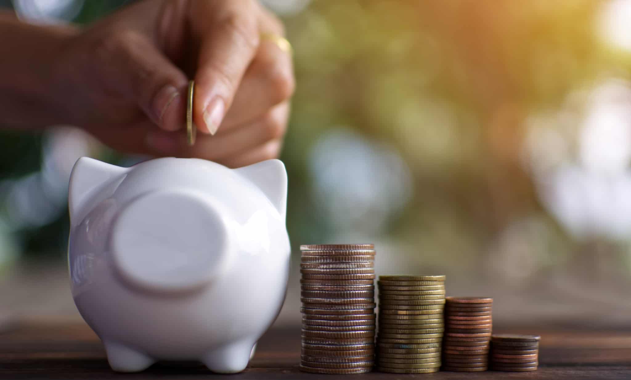 Mão feminina a colocar moedas num mealheiro branco com forma de porquinho