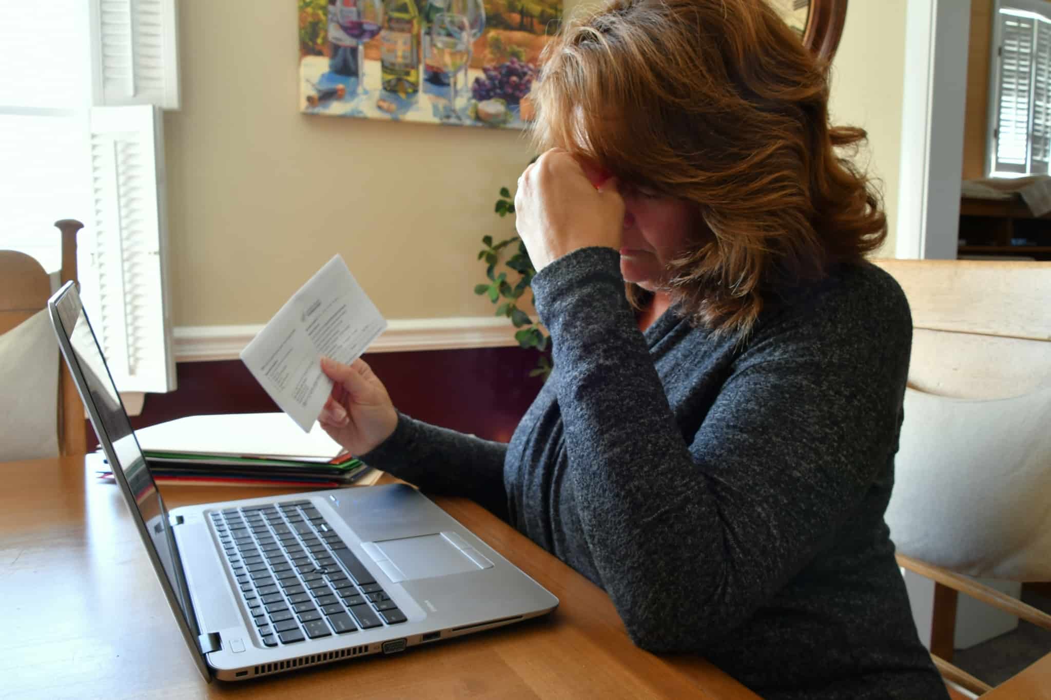 mulher com ar preocupado em frente ao computador, com uma carta numa mão