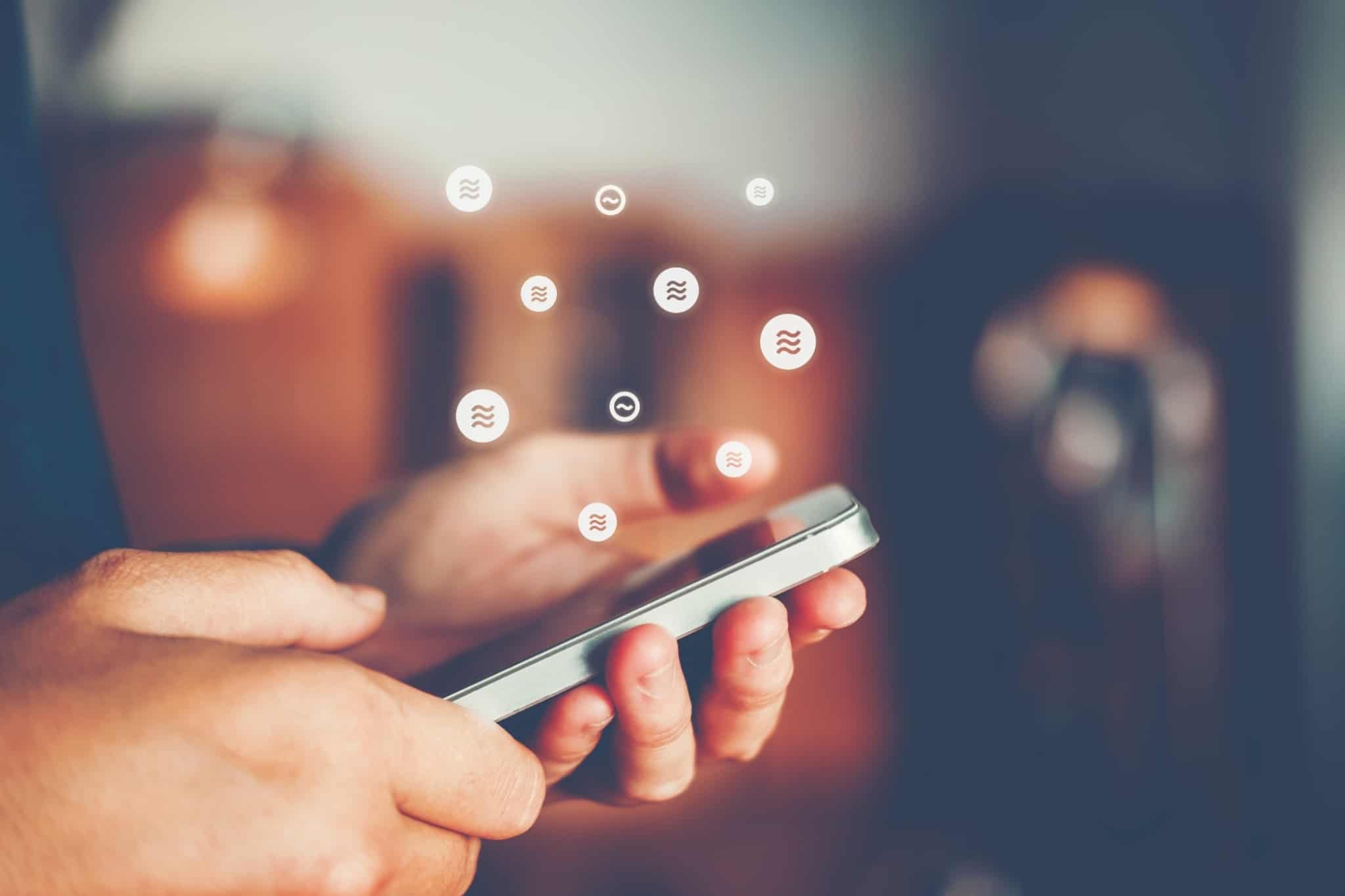 Um telemóvel no meio de umas mãos, rodeado de icons associados às tecnologias