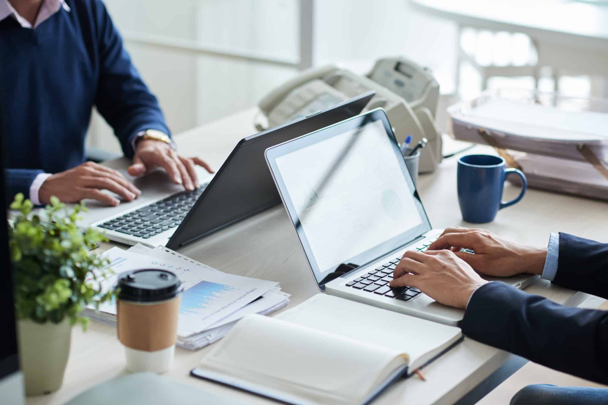 Duas pessoas trabalham num escritório frente em frente. Cada uma com o seu computador portátil