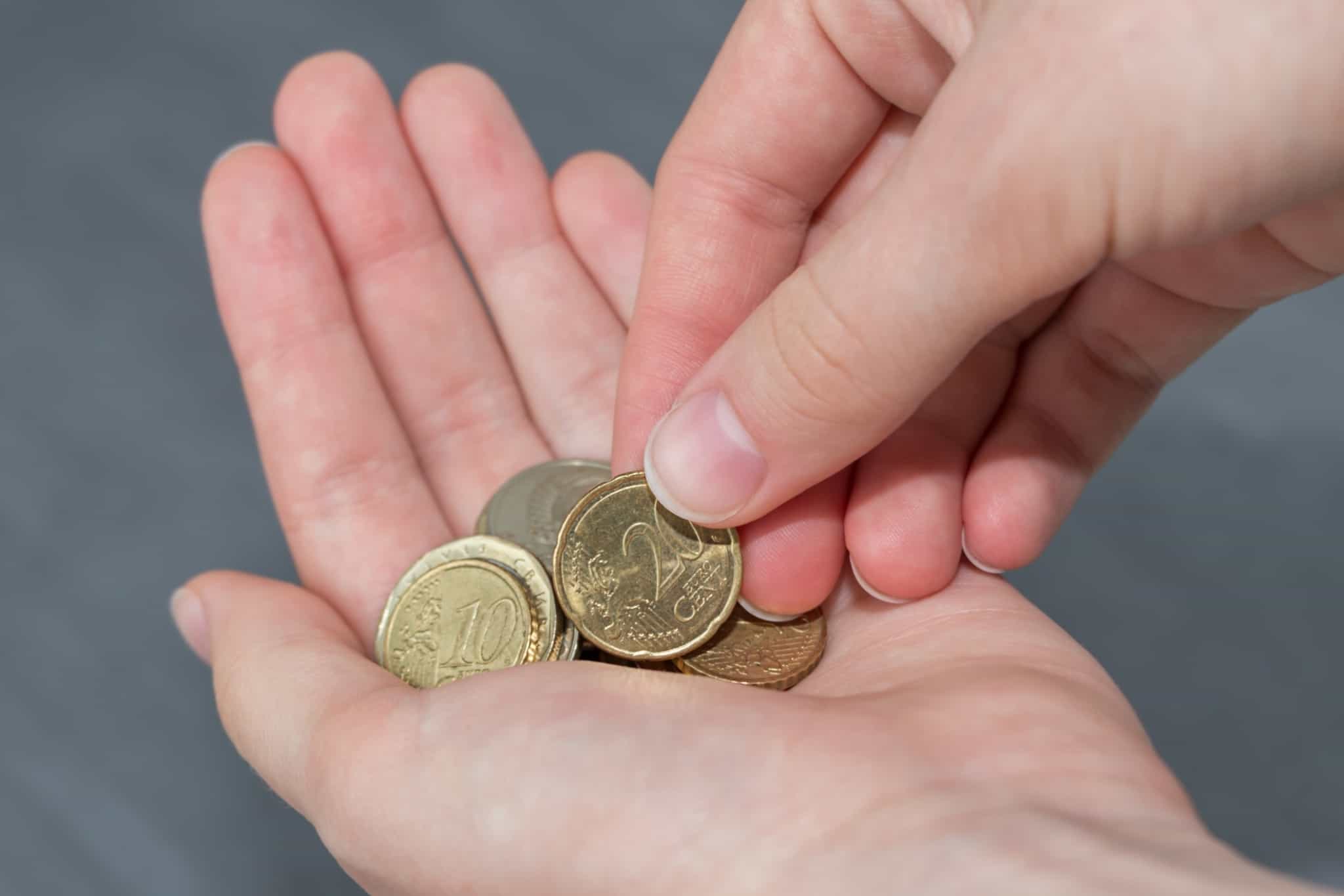 Uma mão a colocar sobre a outra mão uma série de moedas de euro
