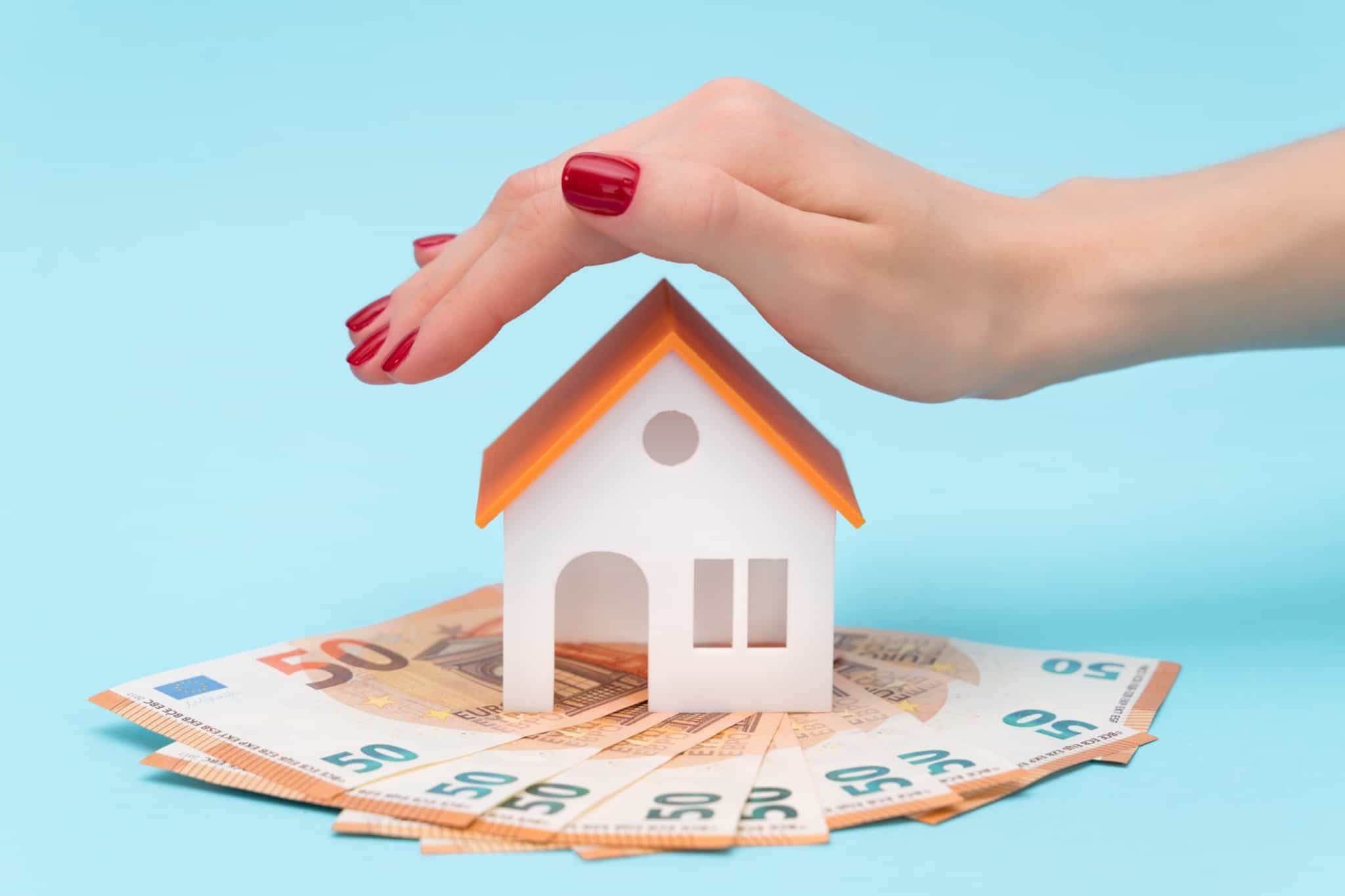 Miniatura de uma casa sobre várias notas de 50 euros e uma mão de mulher por cima