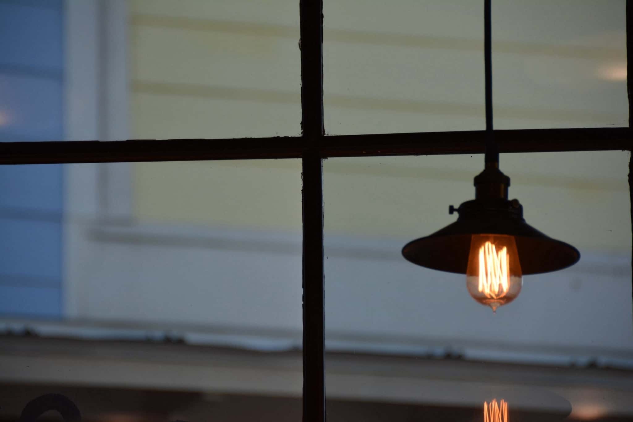 Imagem de um cadeeiro de teto dentro de uma casa. Como pano de fundo está uma janela com com vista para a casa da frente