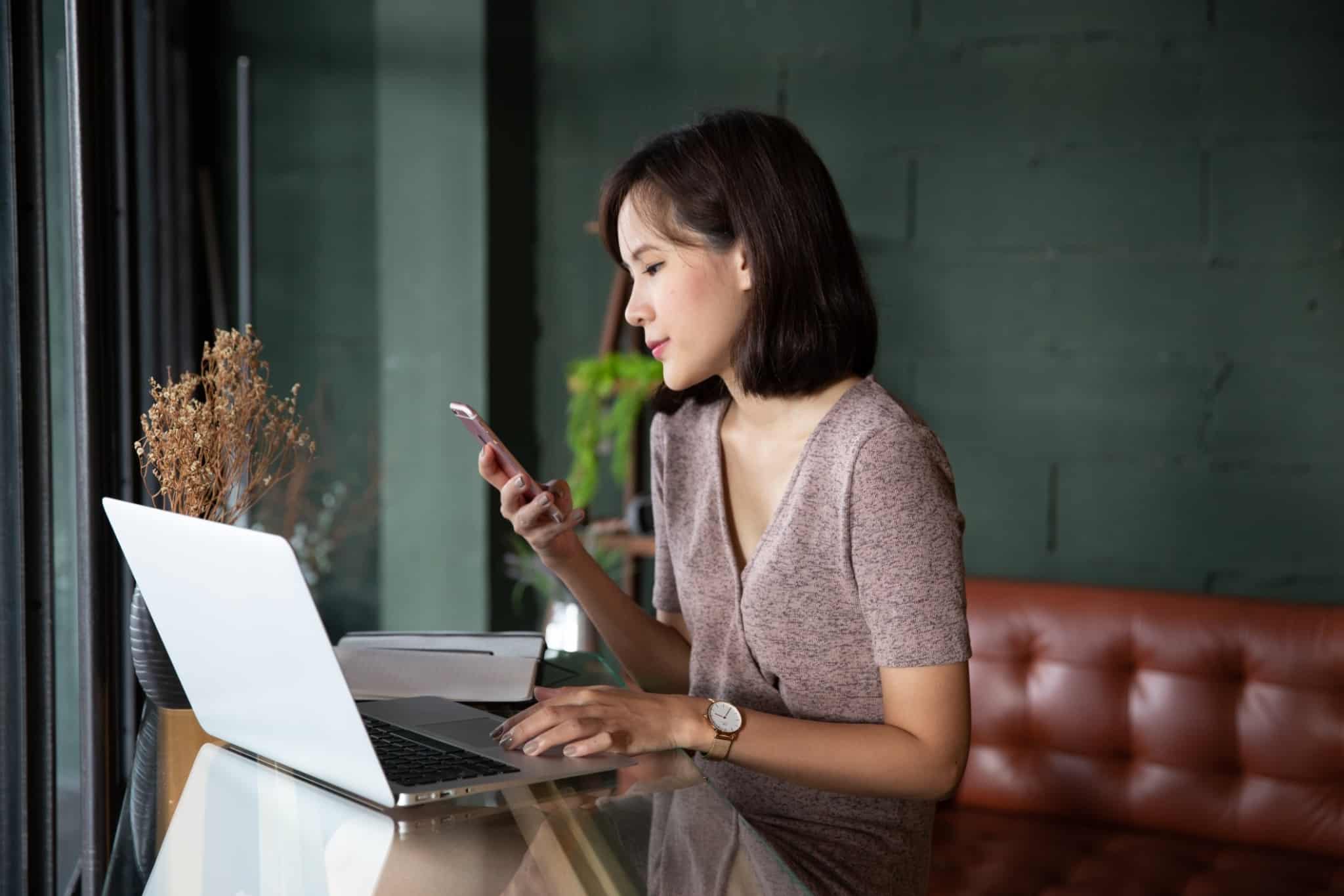 Mulher em frente ao computador e como telemóvel na mão