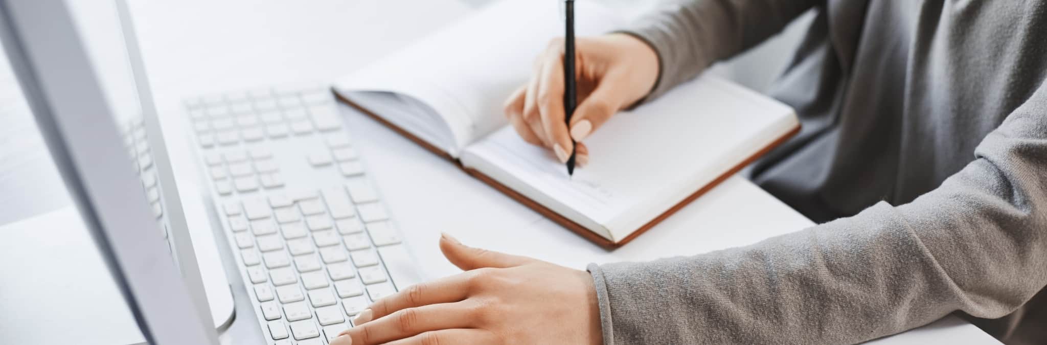 mãos femininas a escrever no teclado e caderno