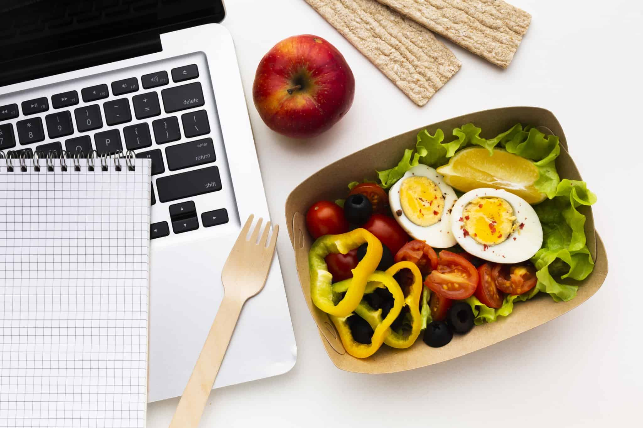 uma embalhagem com uma salada composta por vegetais e ovos ao lado de um computador