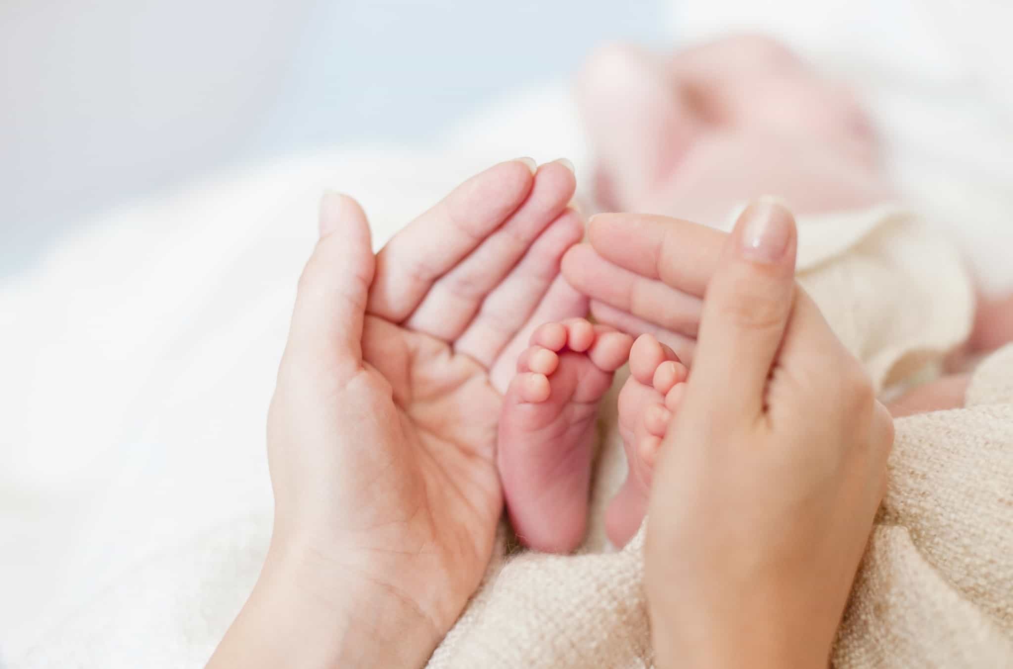 Mãos de uma mãe em torno dos pés de um recém-nascido