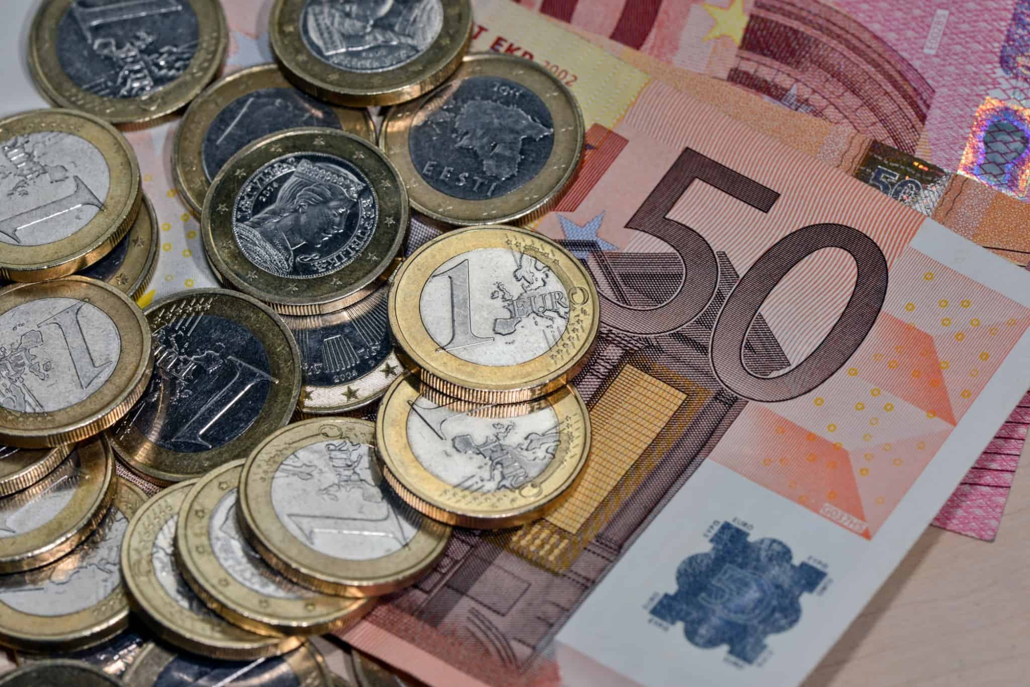 várias moedas de um euro sobre notas de50 euros
