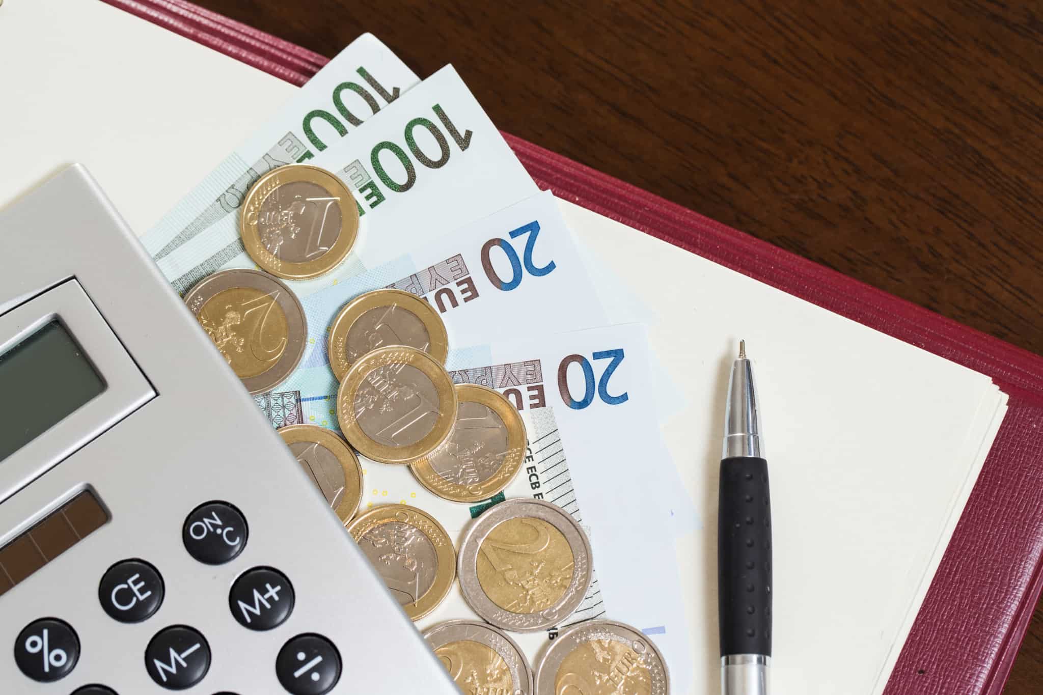 calculadora, várias notas e moedas em cima de um bloco de notas