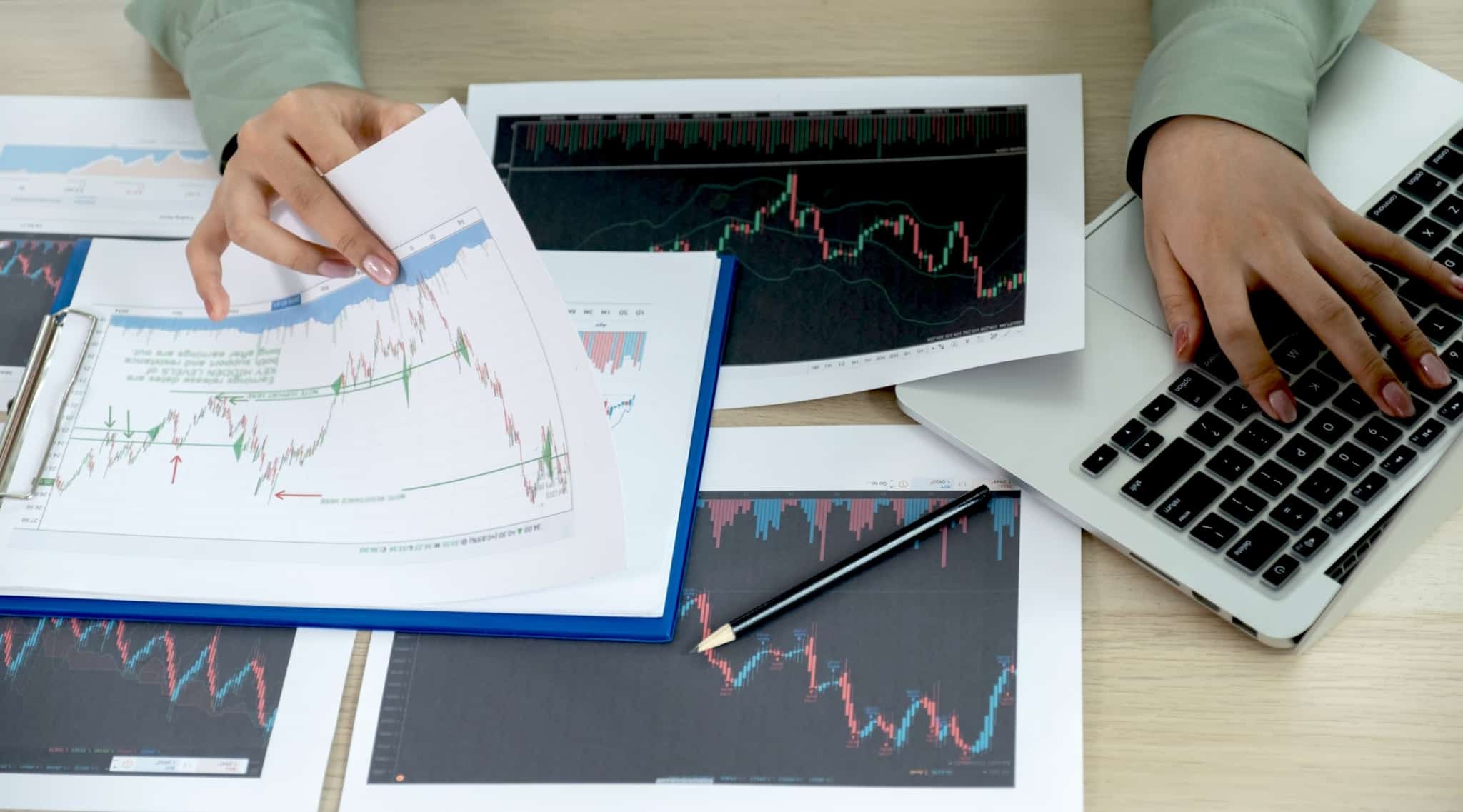 Mãos de uma operadora do mercado bolsista a analisar gráficos ao mesmo tempo que regista informação no computador