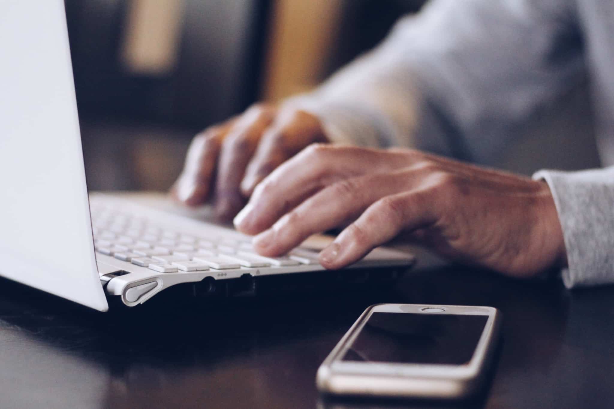 Homem escreve no computador mantendo o telemóvel ao seu lado