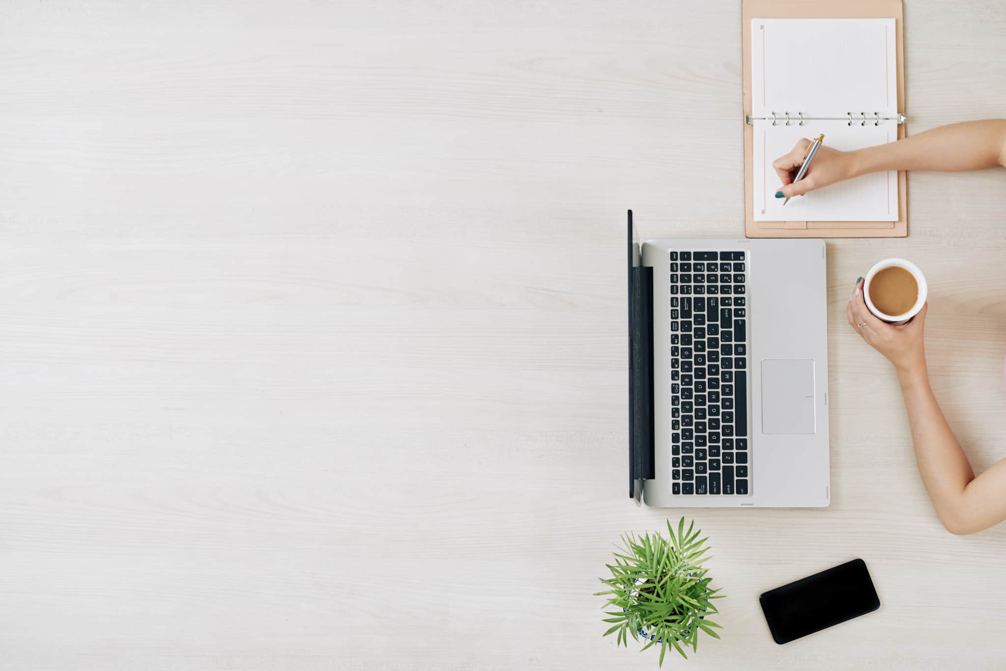 freelancer escreve na sua agenda. À sua frente está o seu portátil e o seu telemóvel
