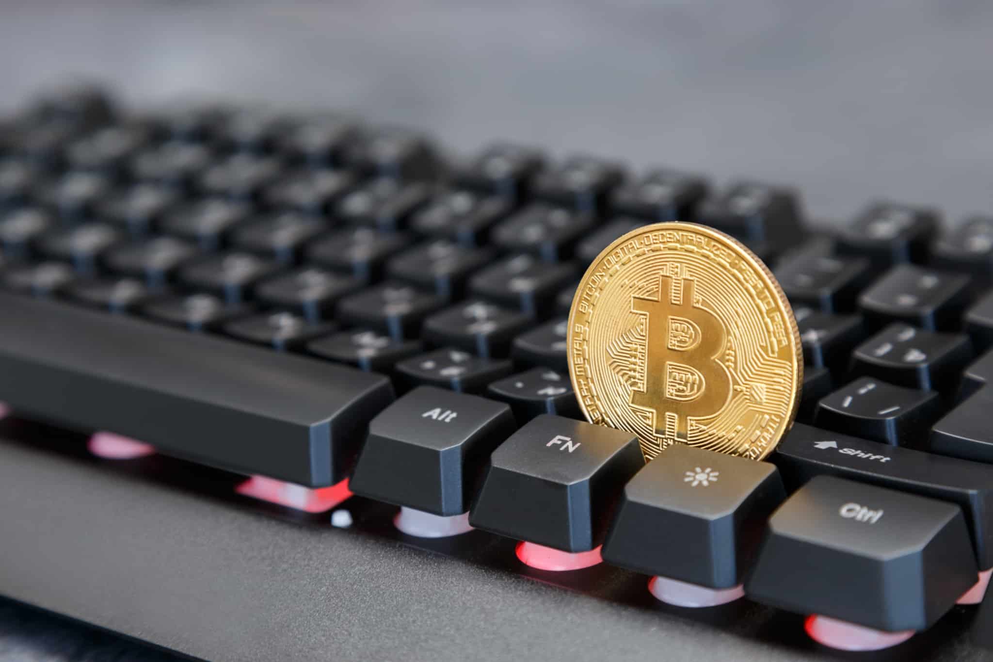 moeda de ouro com o símbolo da bitcoin presa no meio de um teclado de um computador
