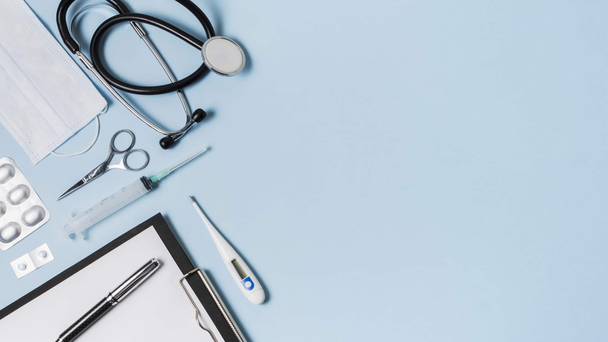 vários instrumentos médicos, como um estetoscópio, uma seringa e um termómetro, em cima de uma mesa
