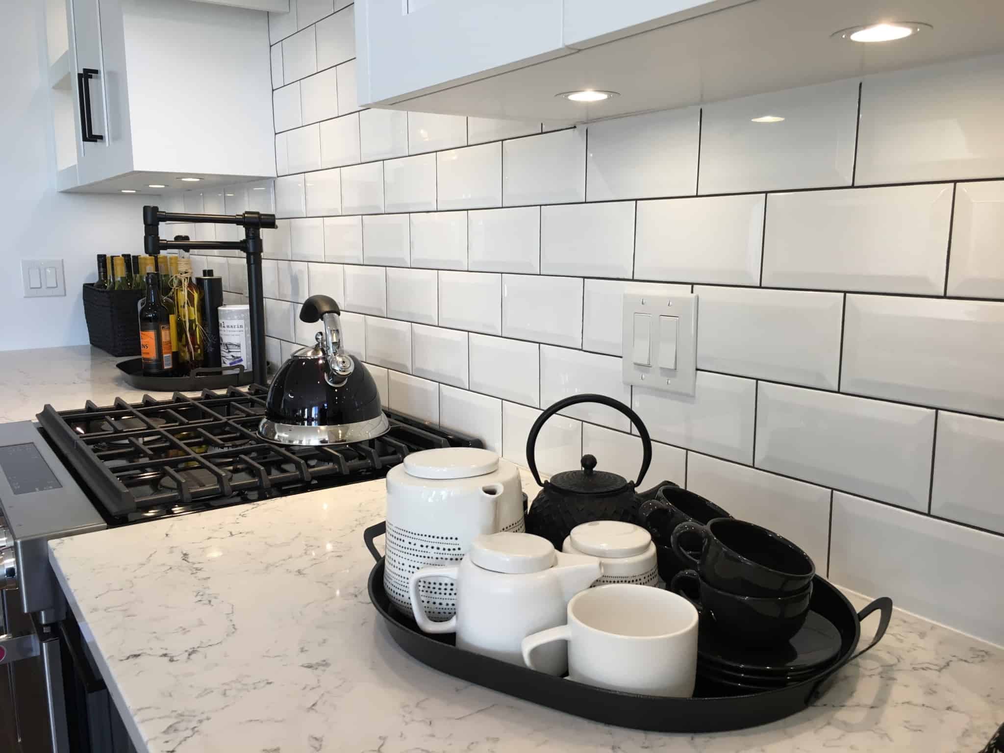 Bancada de uma cozinha onde se vê um tabuleiro com taças de chá. Ao lume está um fervedor com água