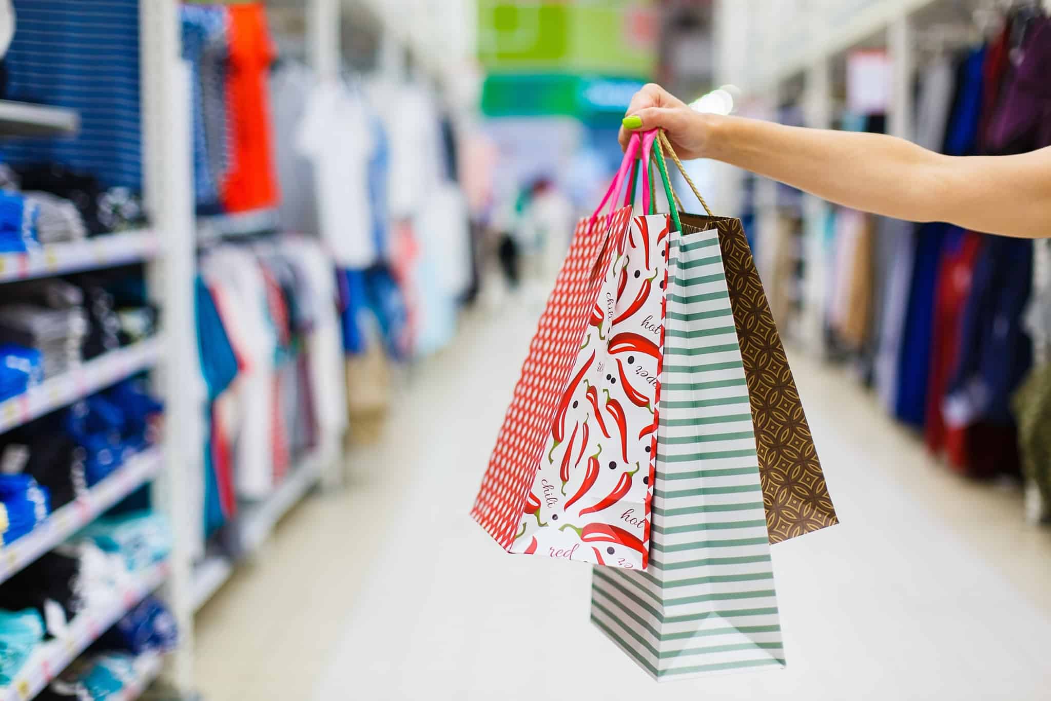 uma mão com três sacos de compras de papel coloridos
