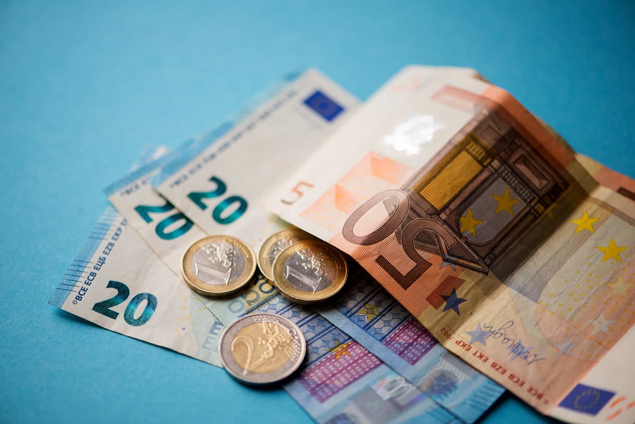 Notas e moedas de euro espalhadas em cima de uma mesa azul