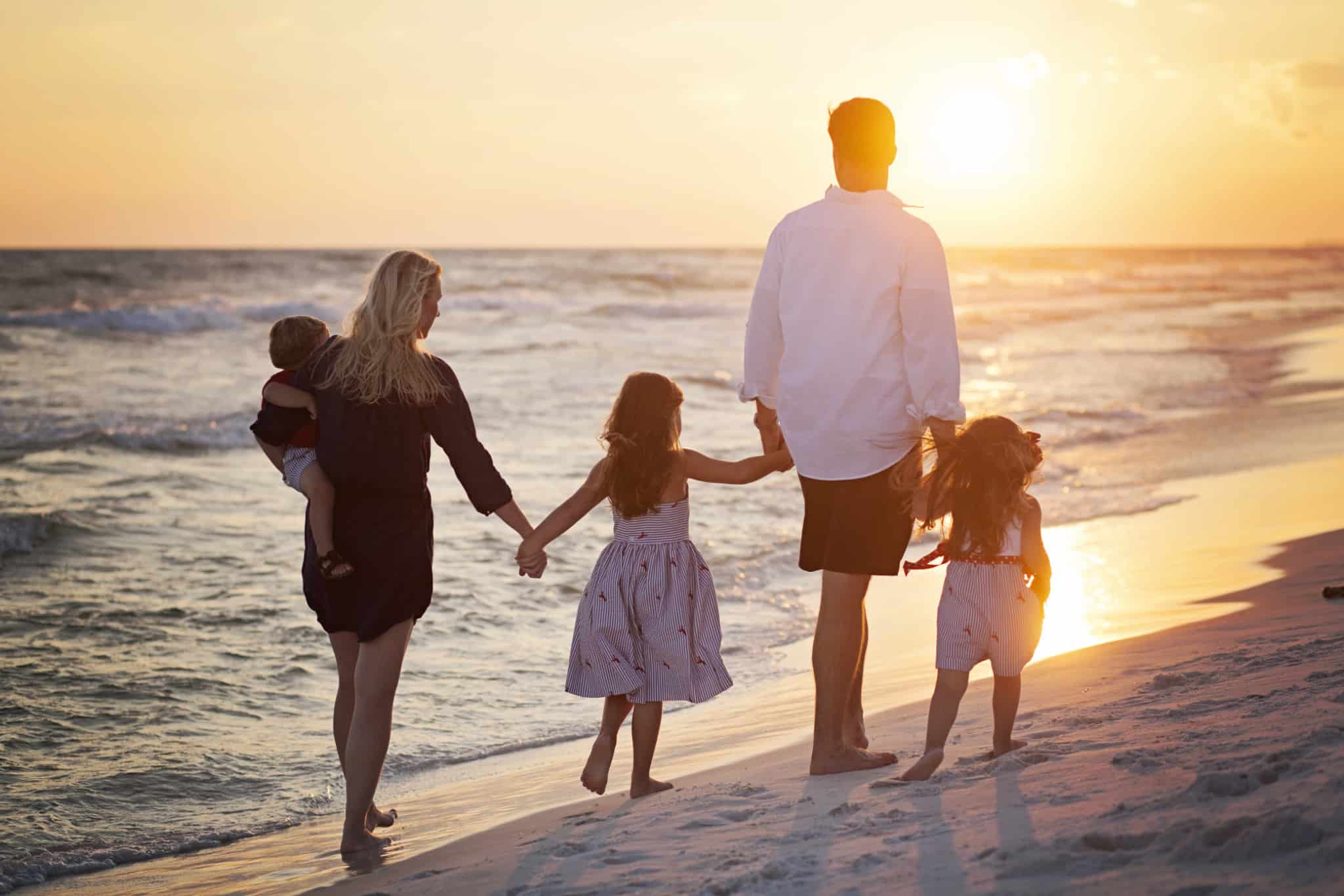 Família (casal de adultos mais três crianças) a passear na praia à beira mar