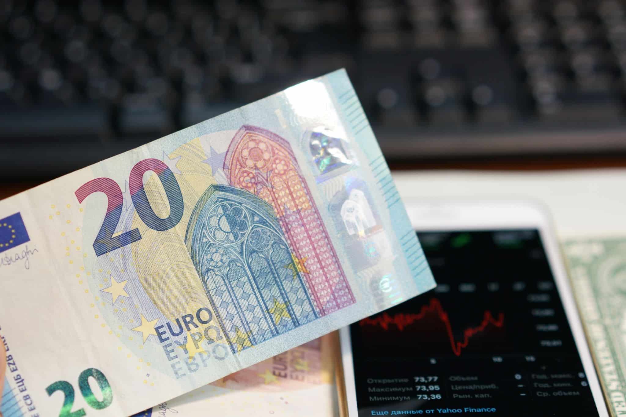 Imagem de uma nota de 20 euros e de um smartphone a mostrar uma aplicação com a bolsa de valores