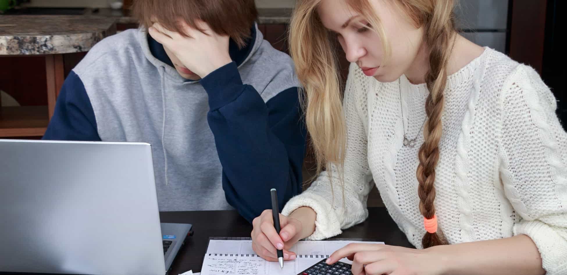 jovem casal faz as contas às suas despesas mensais, consultando documentos, apontando no caderno e usando uma calculadora
