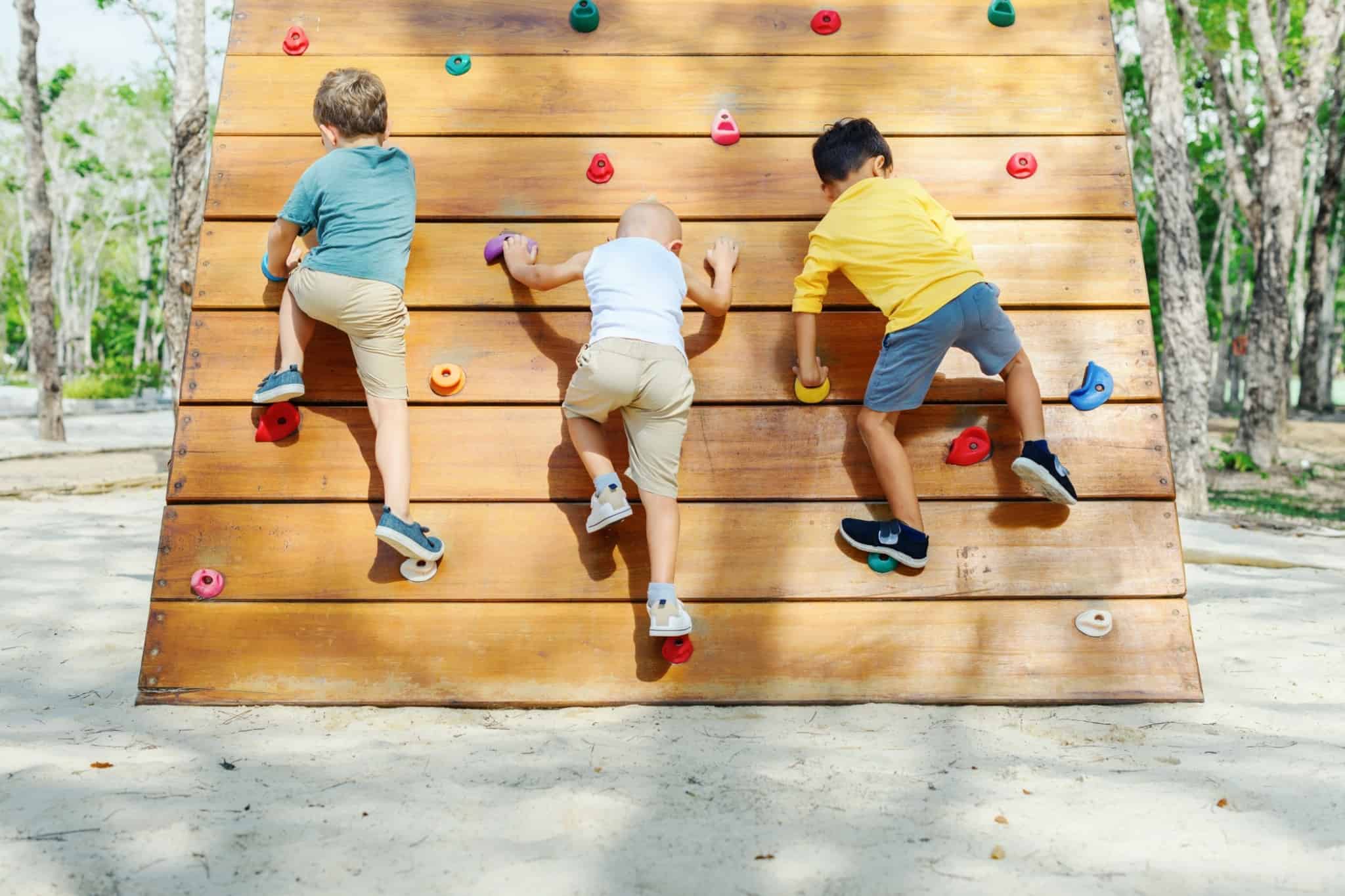 Três crianças escalam uma parede artificial num parque de diversões