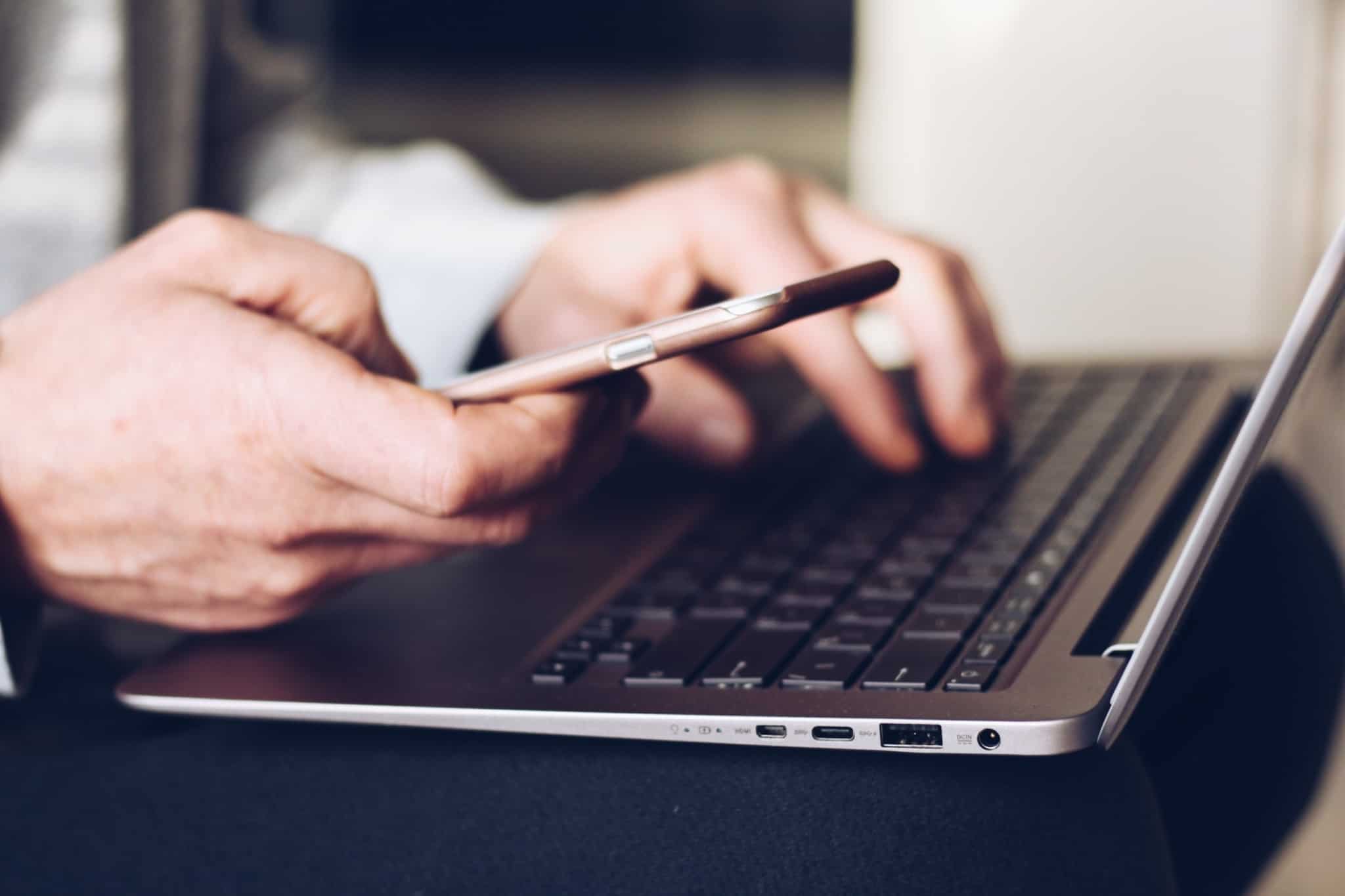 Homem consulta conta bancária através do seu computador ao mesmo tempo que vê o seu telemóvel