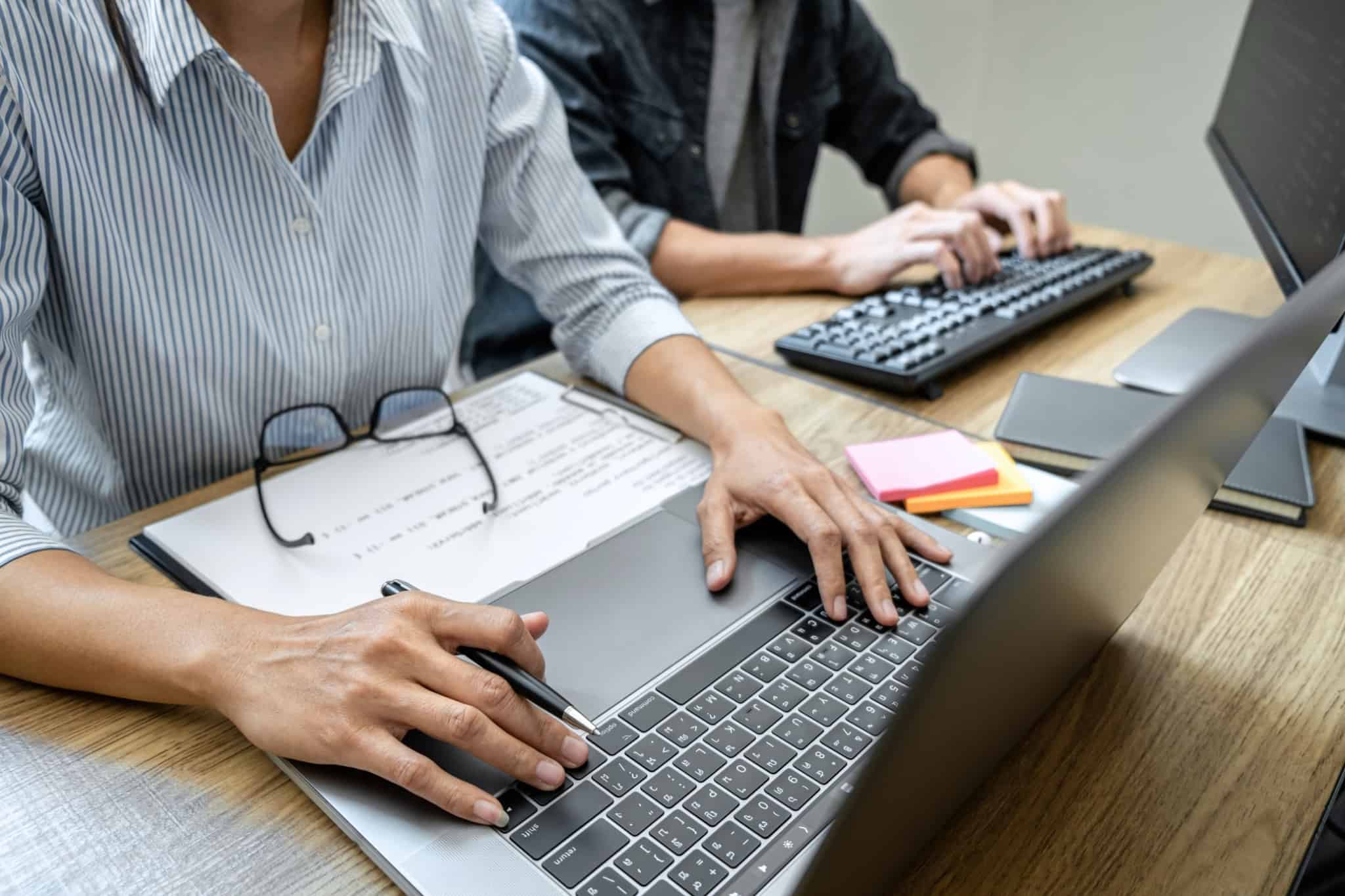 Funcionária trabalha ao computador e ao seu lado tem um colega