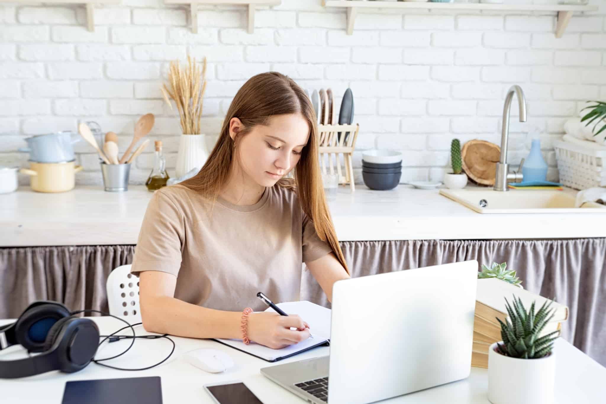 jovem mulher consulta o seu computador na mesa da cozinha