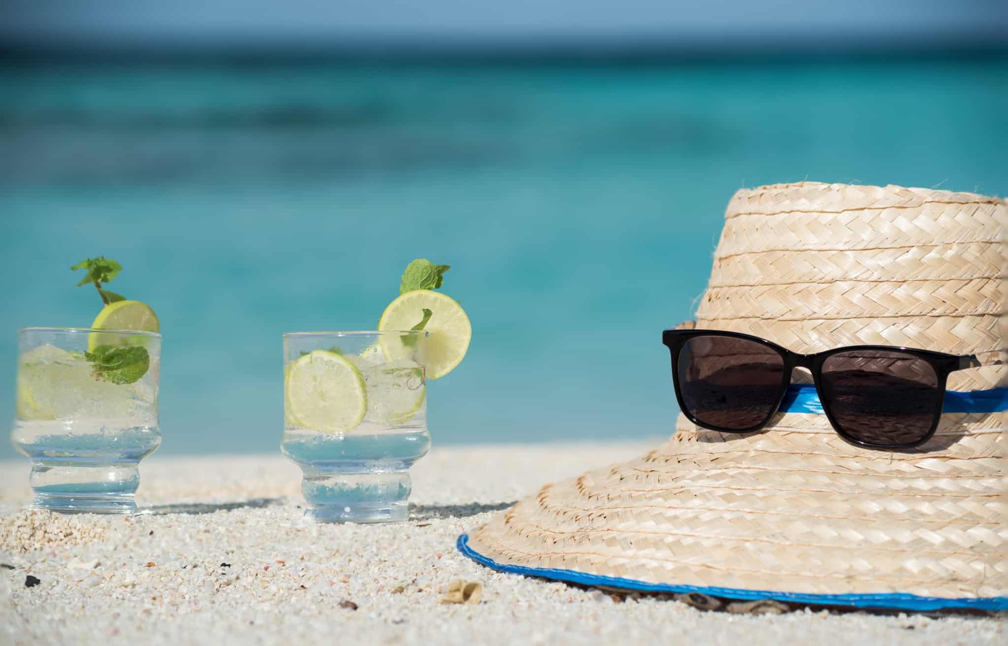 Dois copos com um cocktail pousados à beira da piscina ao lado de um chapéu de sol