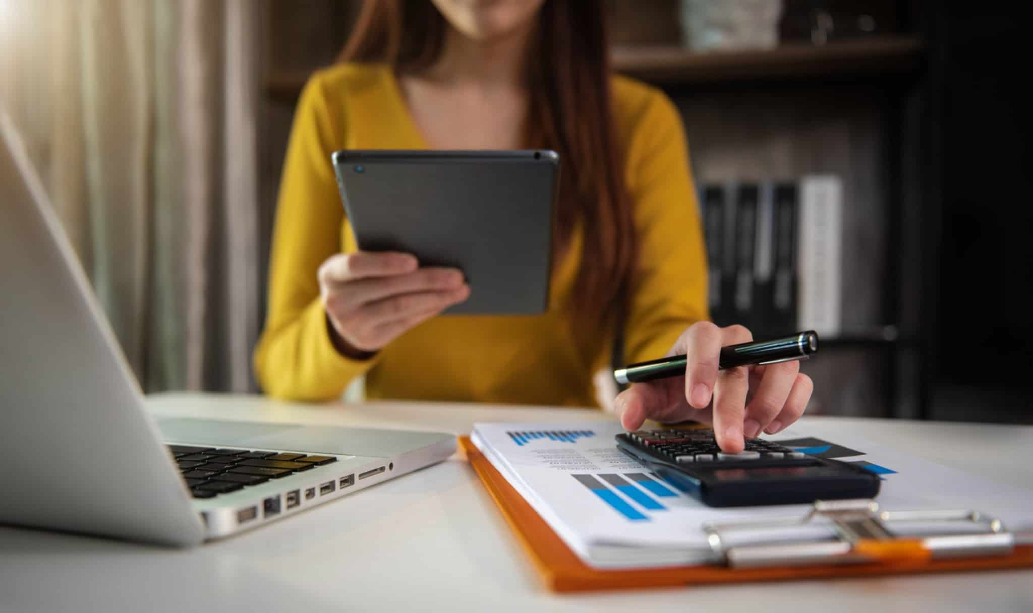 mulher faz contas com a sua calculadora enquanto confirma dados no seu telemóvel