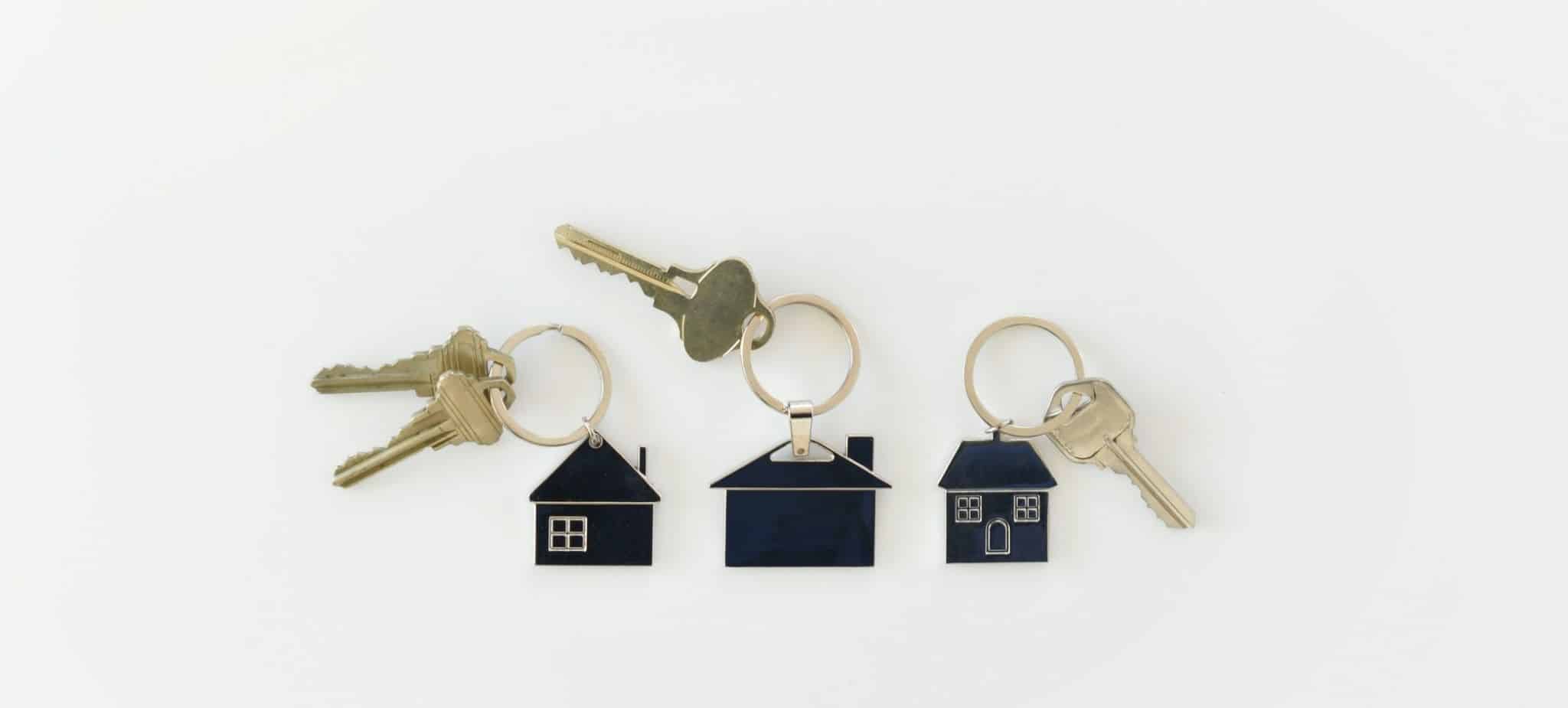 três chaveiros em forma de casa pousados numa superfície branca