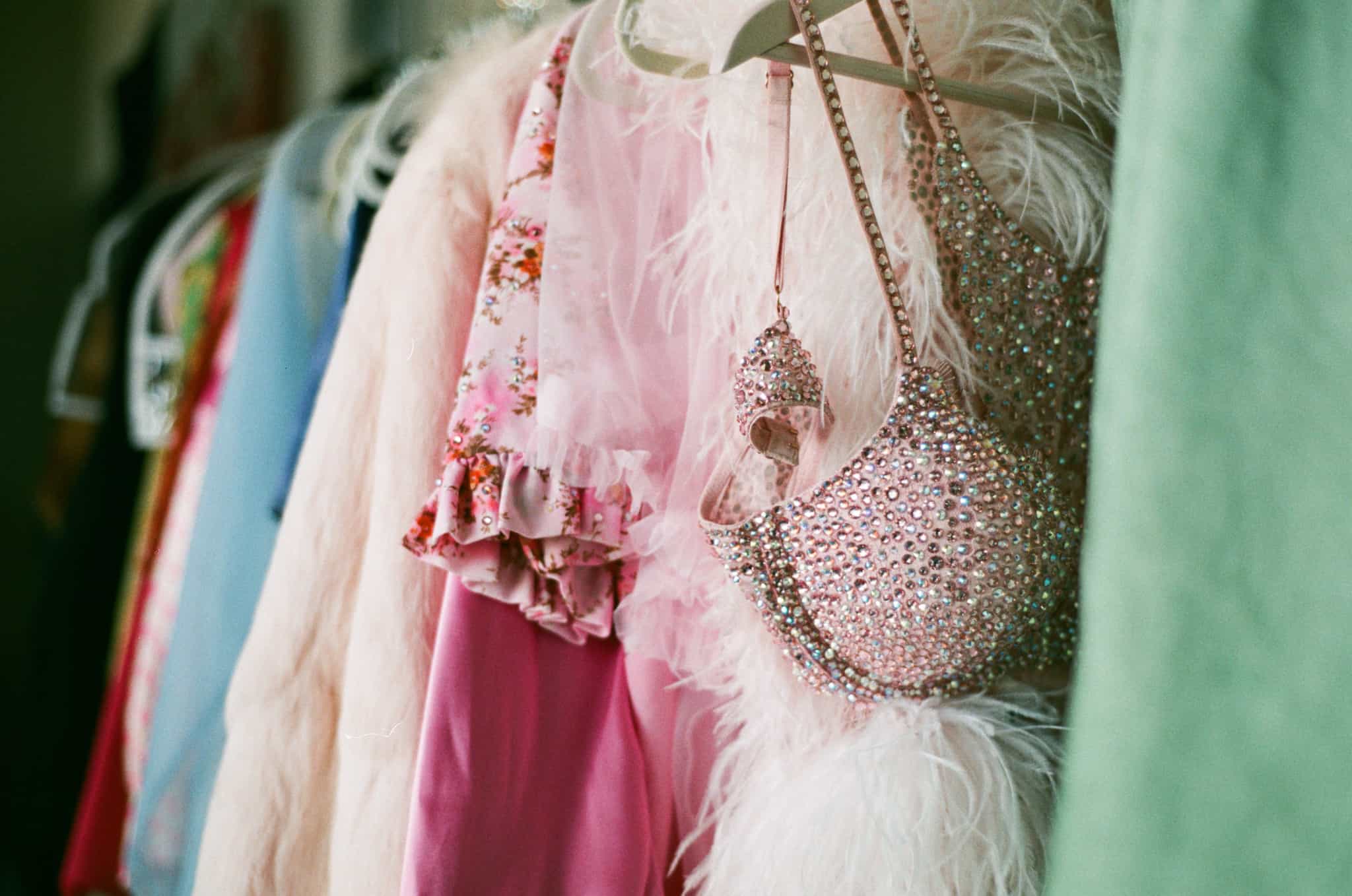 cabide numa loja, cheio de roupa vintage, colorida e com alguns acessórios brilhantes, de época.