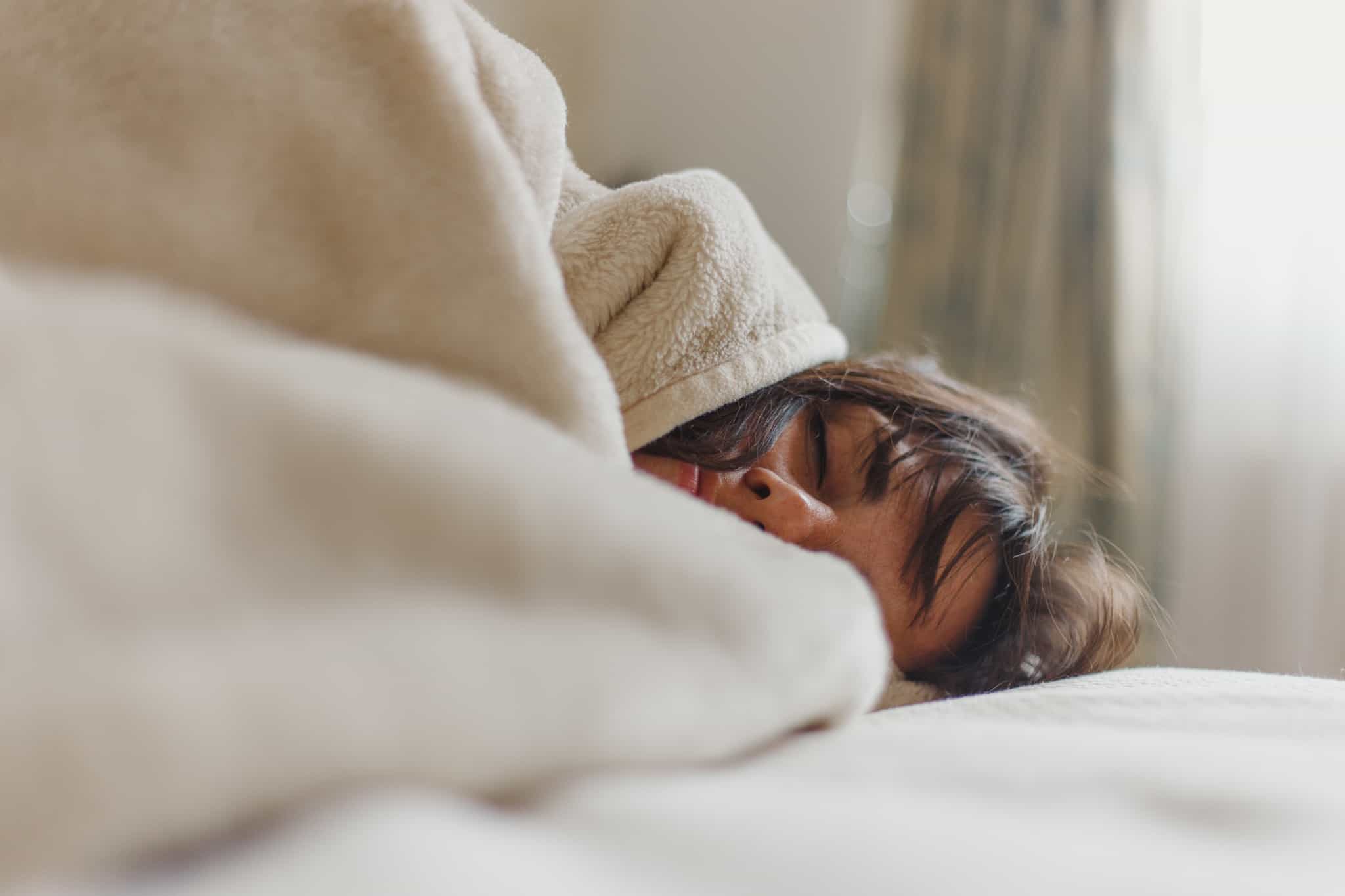 jovem mulher dorme, enroscada em lençóis e manta, com ar muito relax e confortável