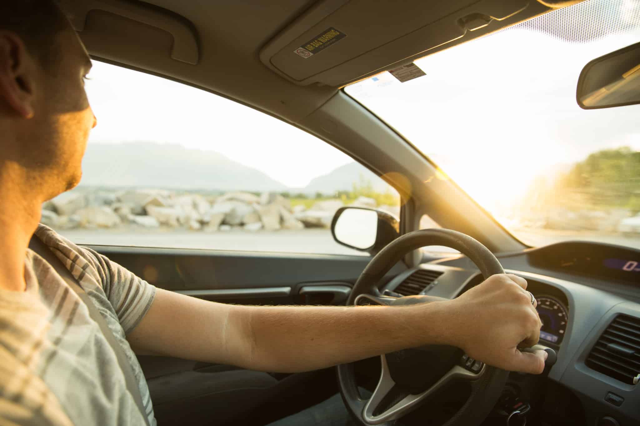 jovem homem ao volante do seu automóvel, num dia ensolarado.