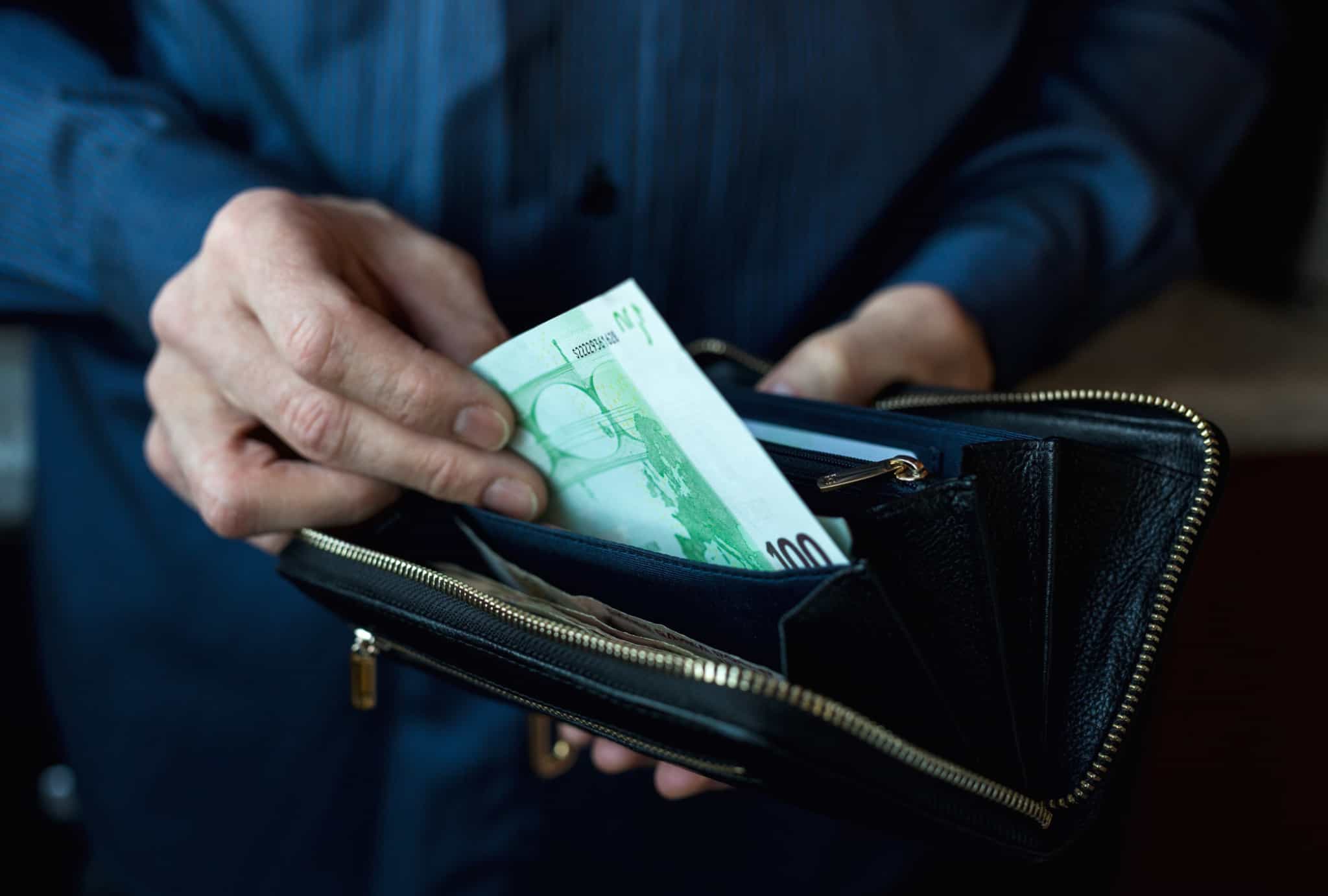 Mãos de homem a guardar uma nota de 100 euros numa carteira, reparando que já não tem mais dinheiro até ao final do mês