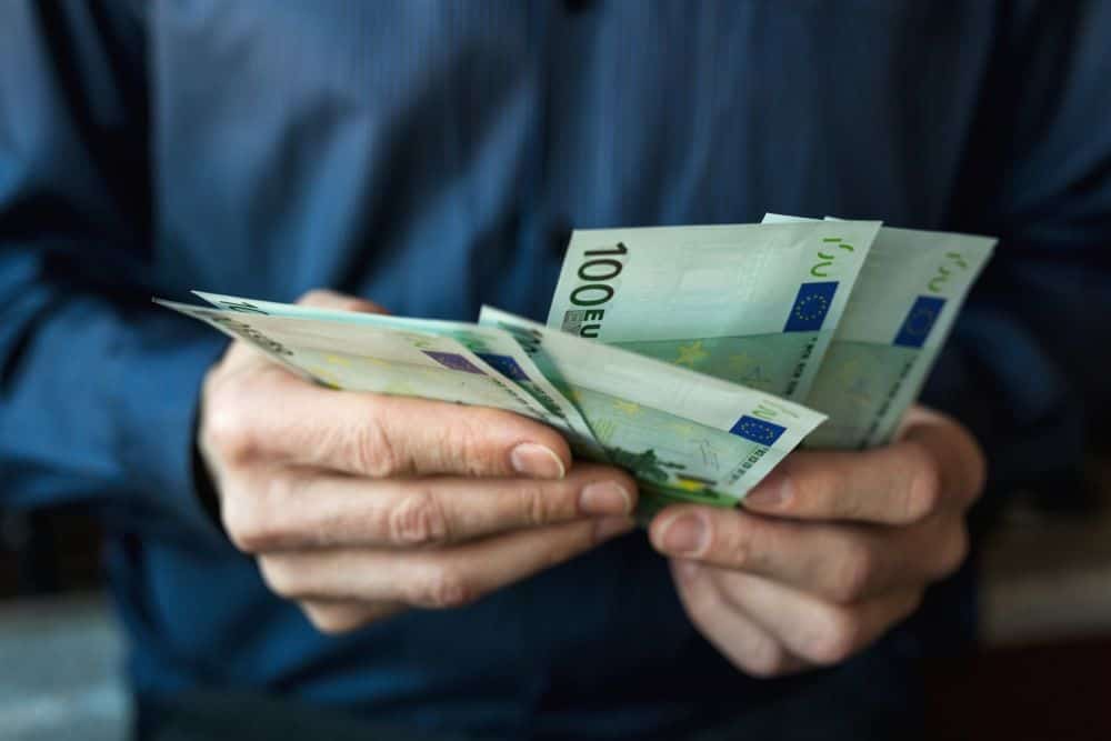 Mãos de homem com várias notas de 100 euros na mão a usar o subsídio de férias.
