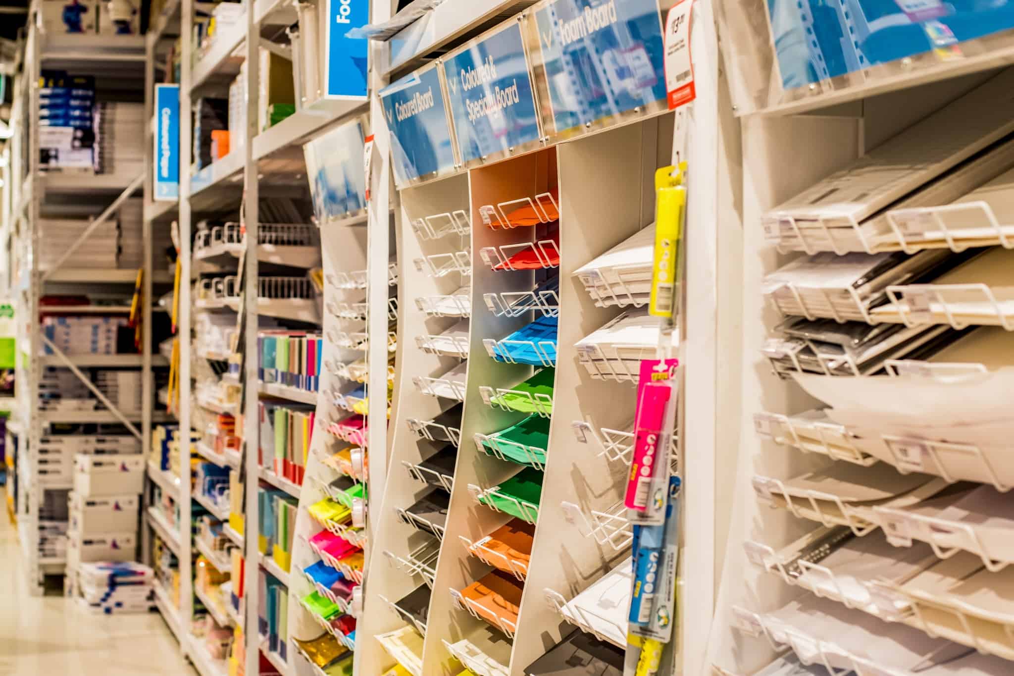 Poupar no regresso às aulas. Estantes de uma superfície comercial com as prateleiras cheias de materiais escolares, como cartolinas de todas as cores e feitios.