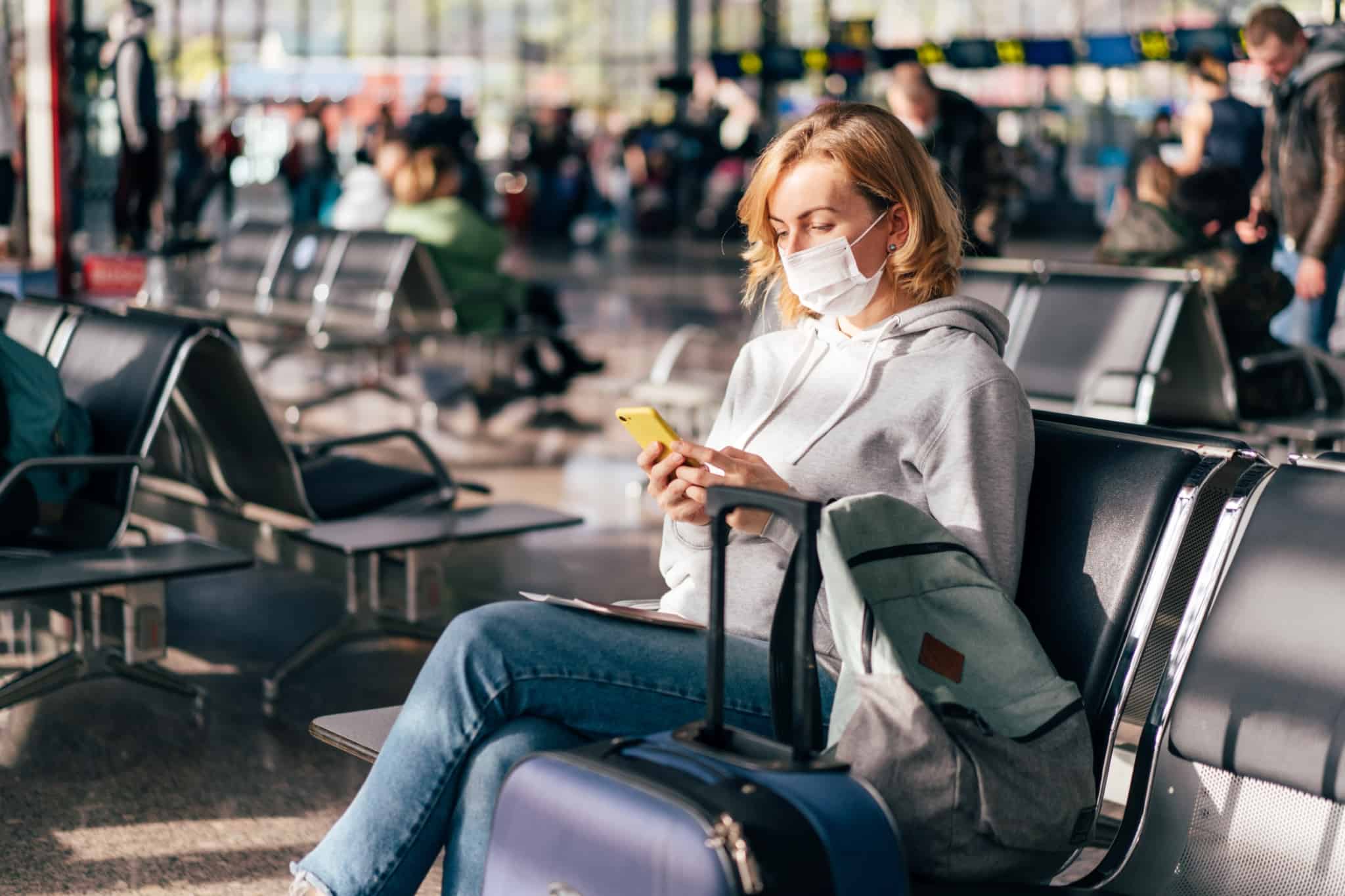 Mulher sentada num aeroporto a consultar no seu telemóvel informação sobre o Cartão Europeu de Seguro de Doença