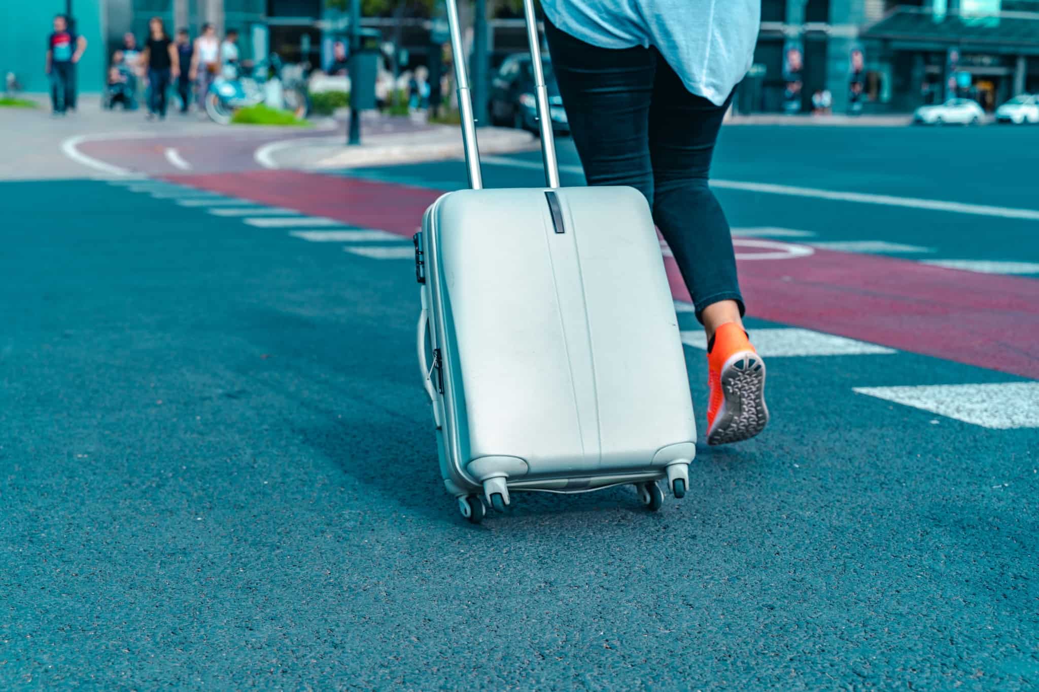 jovem estudante parte para o programa Erasmus. Dirige-se ao aeroporto, para uma entrada com mais jovens a aguardar, arrastando a sua mala de viagem.