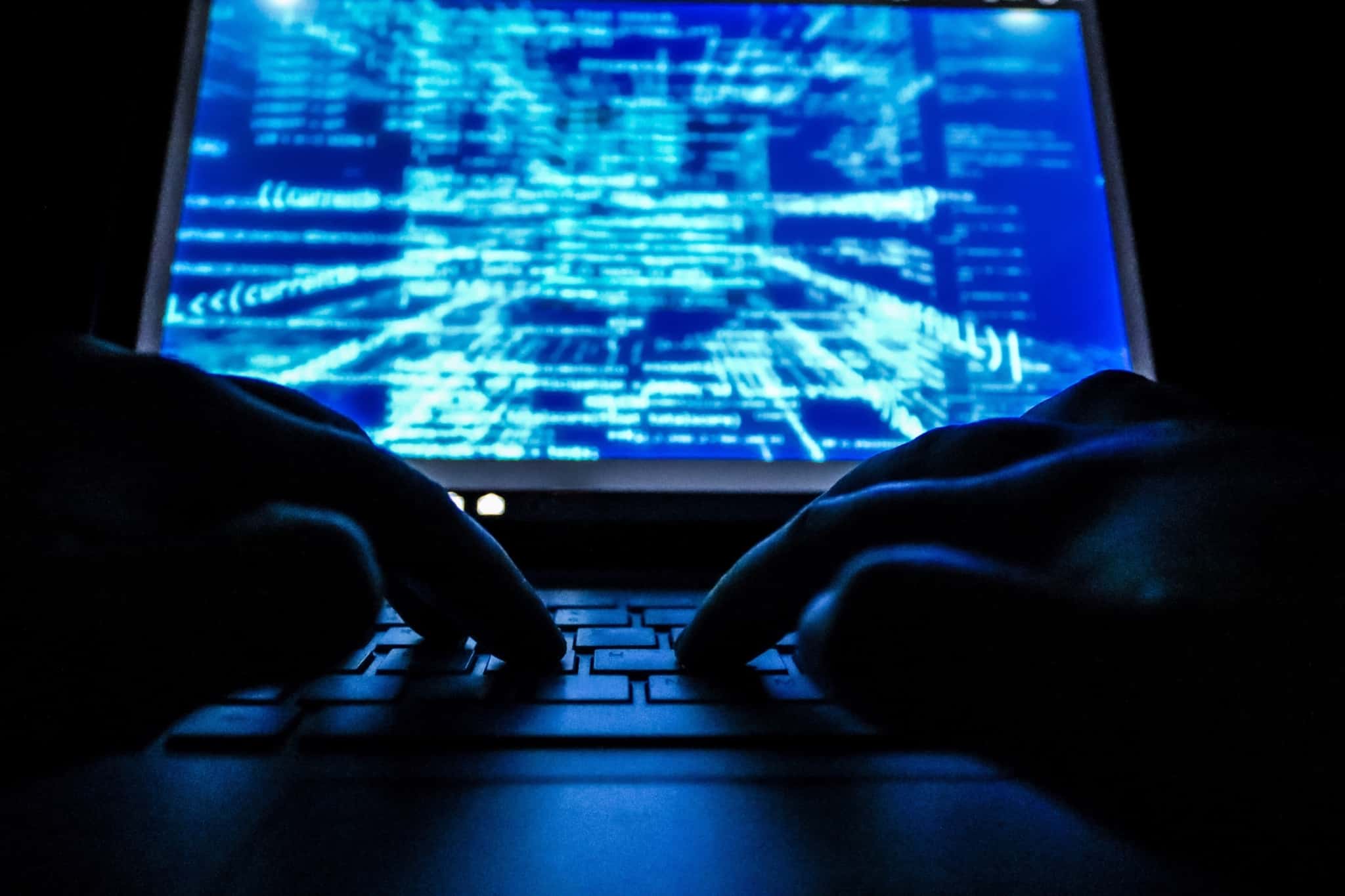 foto ilustrativa do cibercrime com uma imagem escura, só com umas mãos num teclado do computador enquanto se visualizam estruturas informáticas no ecran