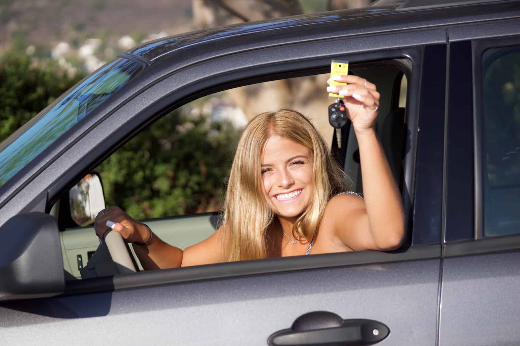 jovem mulher, muito sorridente, mostra à janela do seu primeiro carro, as chaves do veículo