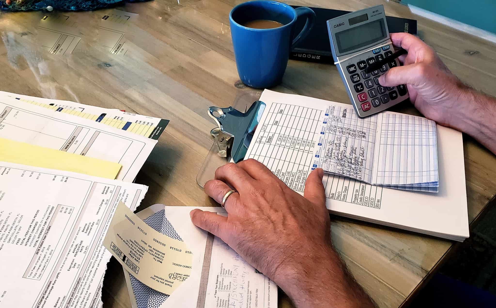 homem, de calculadora na mão, faz contas, revendo todas as contas e despesas que tem.