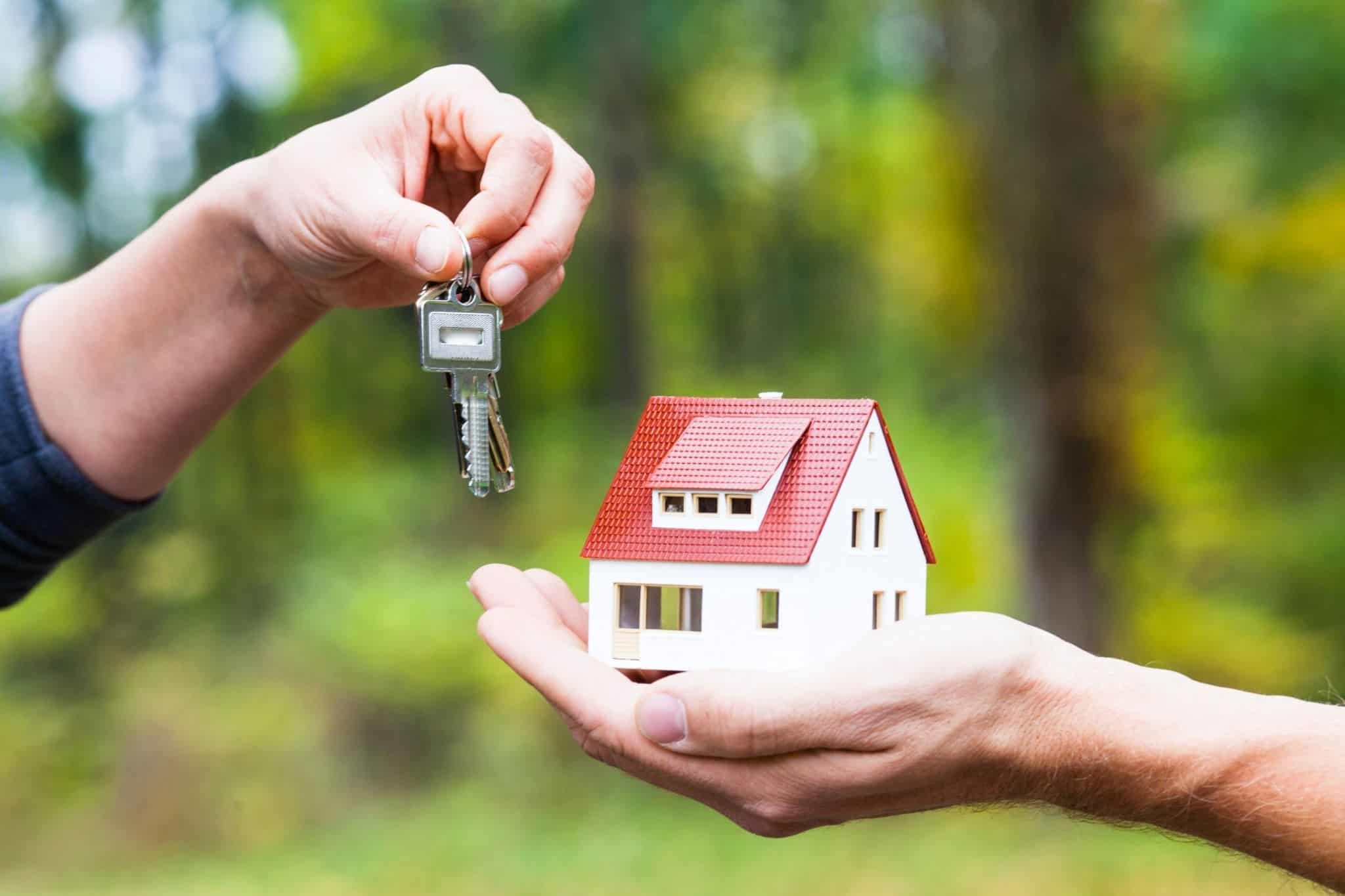 Uma mão agarra numa chave e outra numa casa em miniatura a evcar o processo de compra de casa